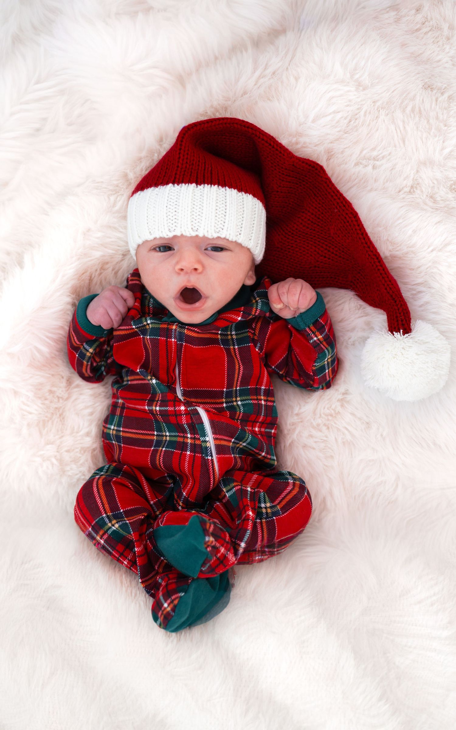 A baby wearing red plaid pajamas and a red Santa hat lies on white fluffy blanket in three similar holiday poses.