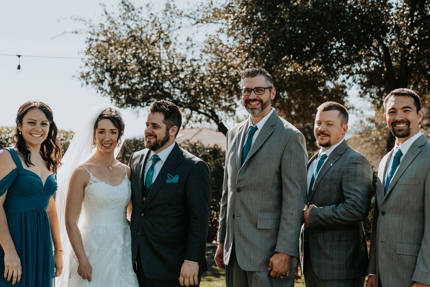 Wedding party lined up outdoors wearing navy and grey formal attire.