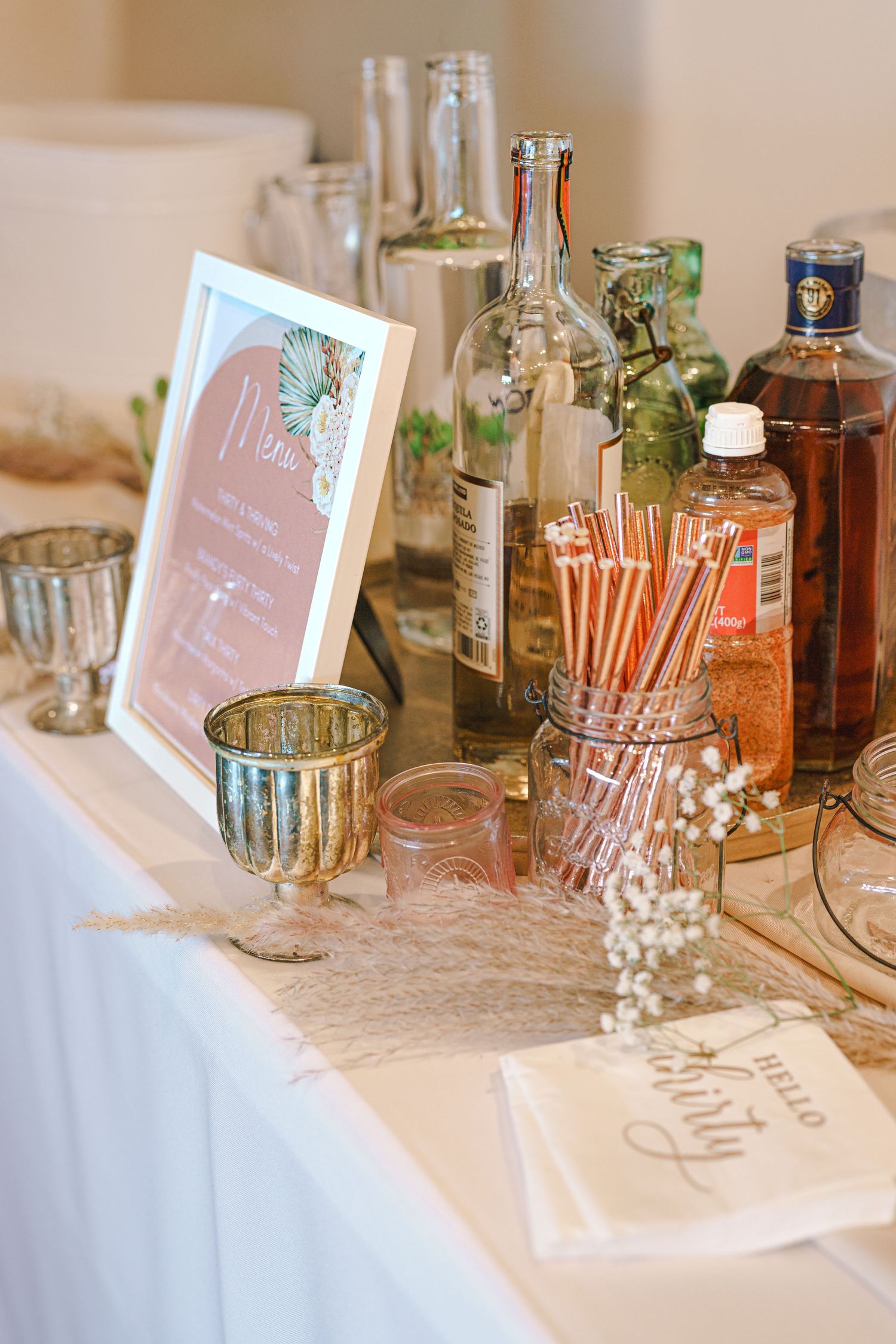 Rustic bar setup with vintage glass bottles, straws and decorative menu display on lace tablecloth. Session in Phoenix Arizona