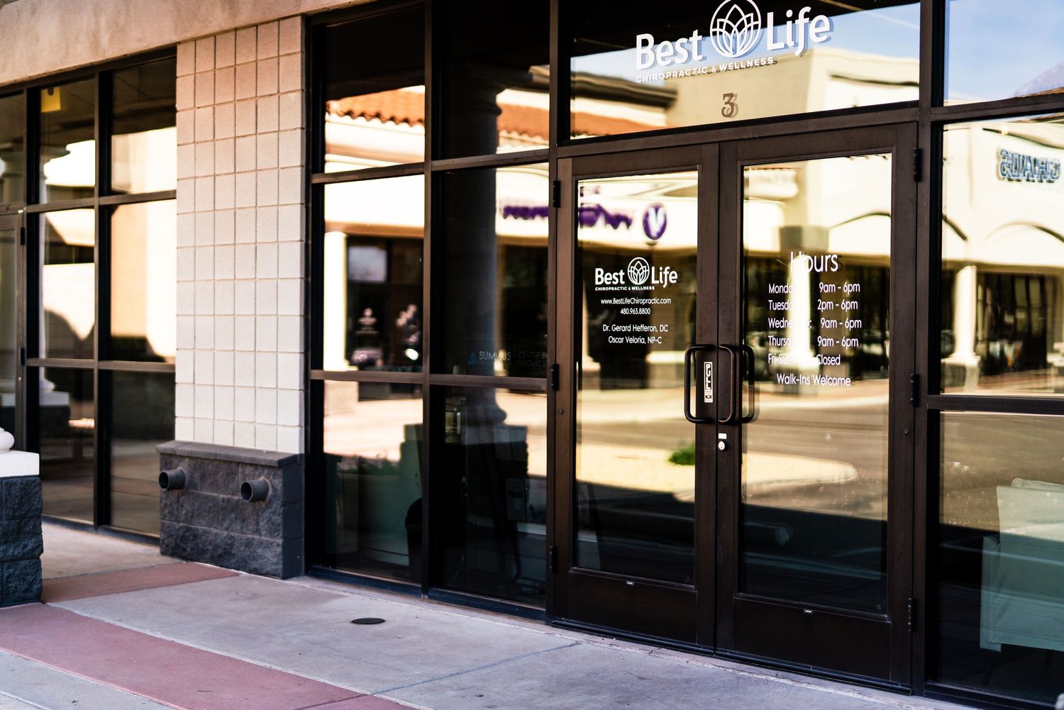 A storefront view of a retail strip mall with beige tiled walls and glass windows during daytime.