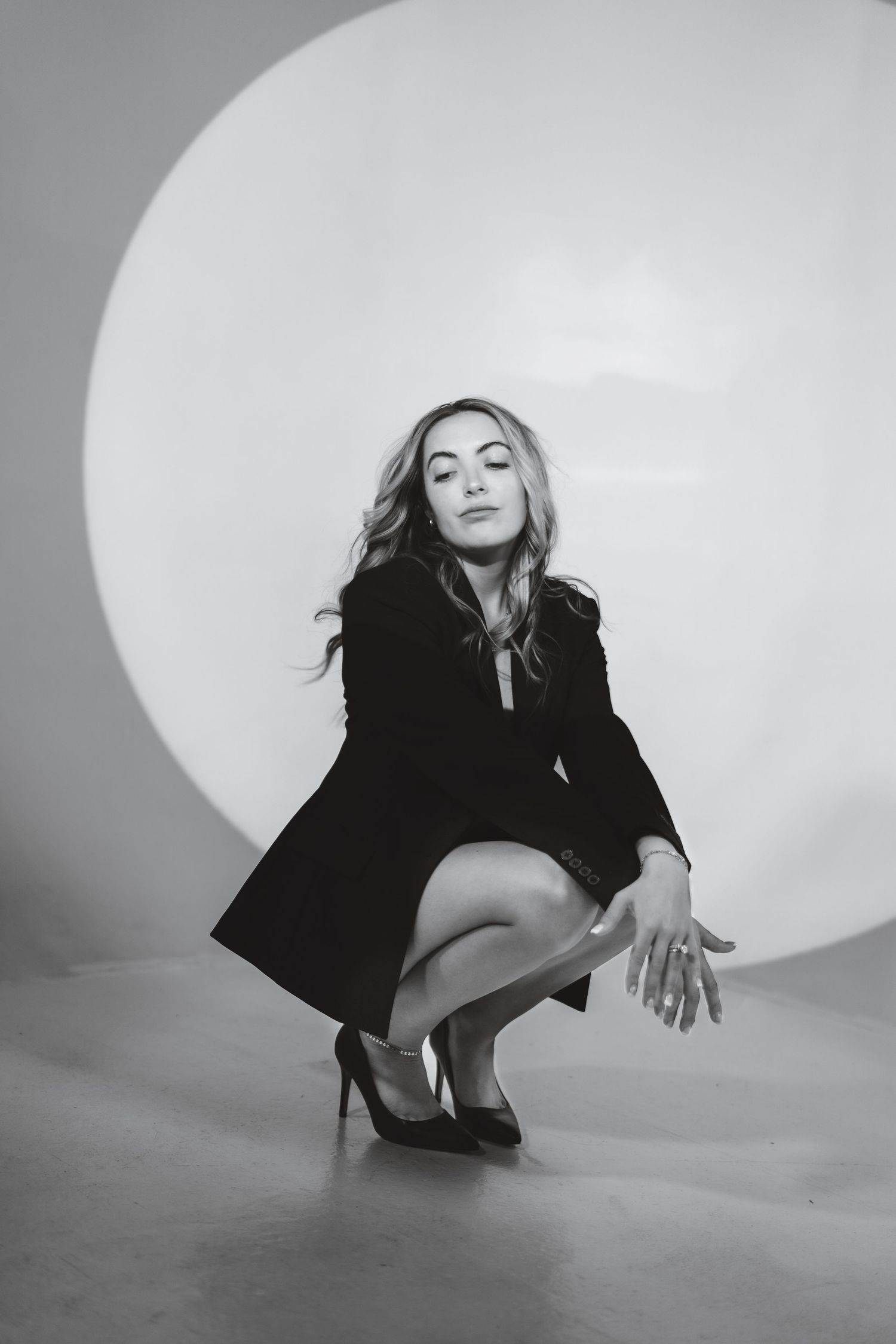 Artistic black and white portrait of someone in a black dress crouching elegantly against a circular backdrop.