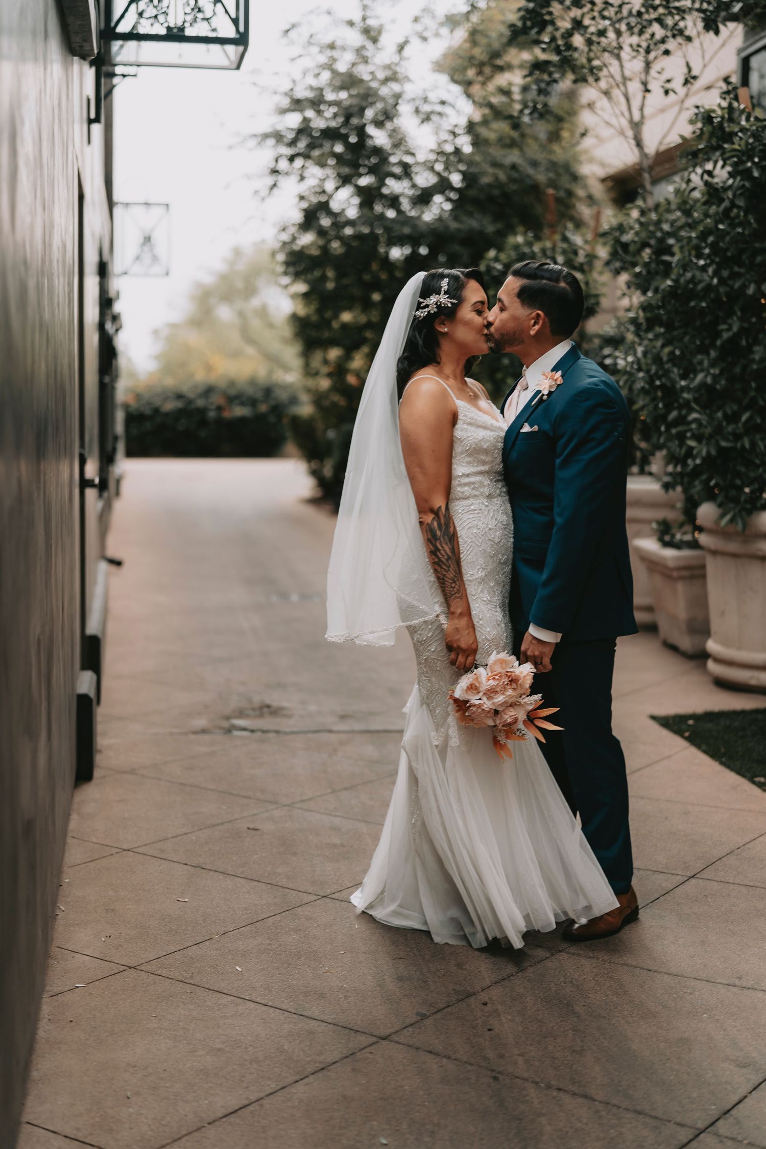 Wedding couple kissing in an outdoor courtyard with stone planters and architectural details.