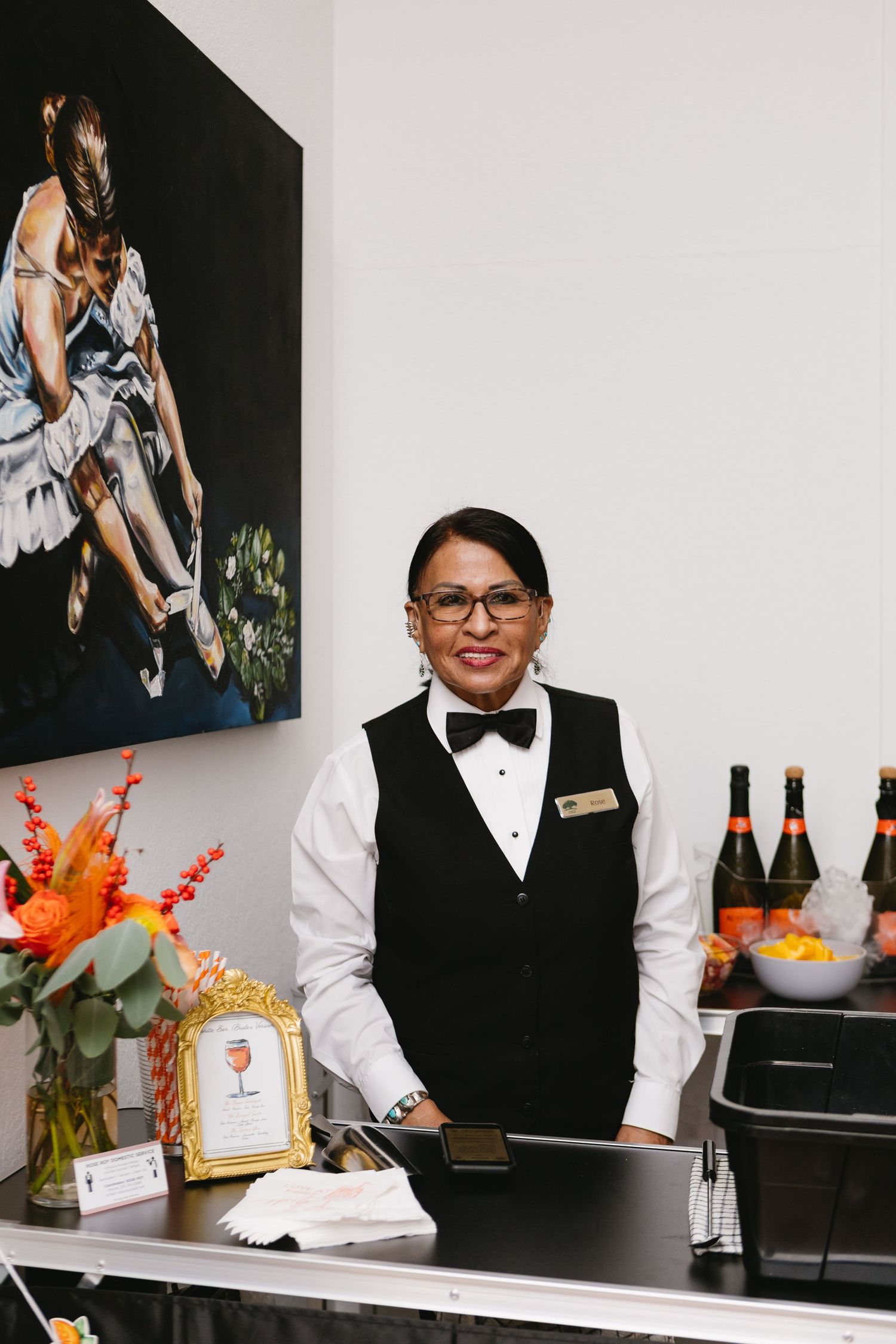 Restaurant staff in formal black and white attire prepare drinks and service items at an elegant bar counter.