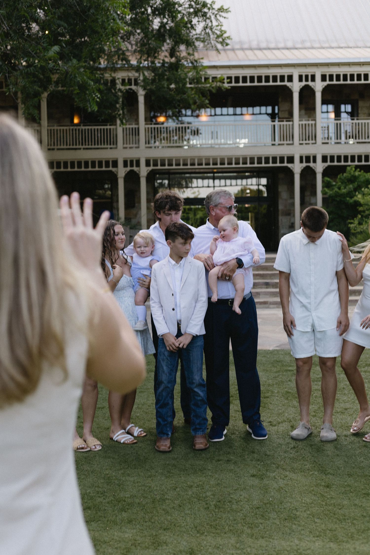 Multi-generational family group posing together on lawn outside elegant historic building.