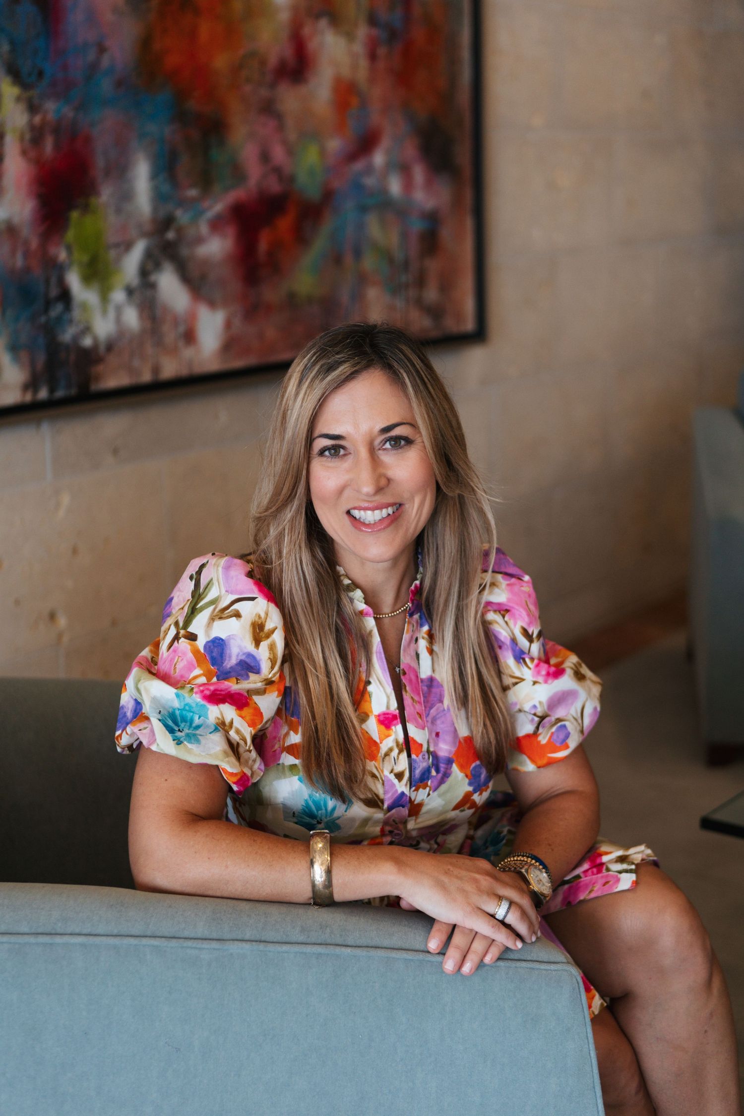 Person in a colorful floral dress poses on a gray couch with vibrant abstract art in the background.