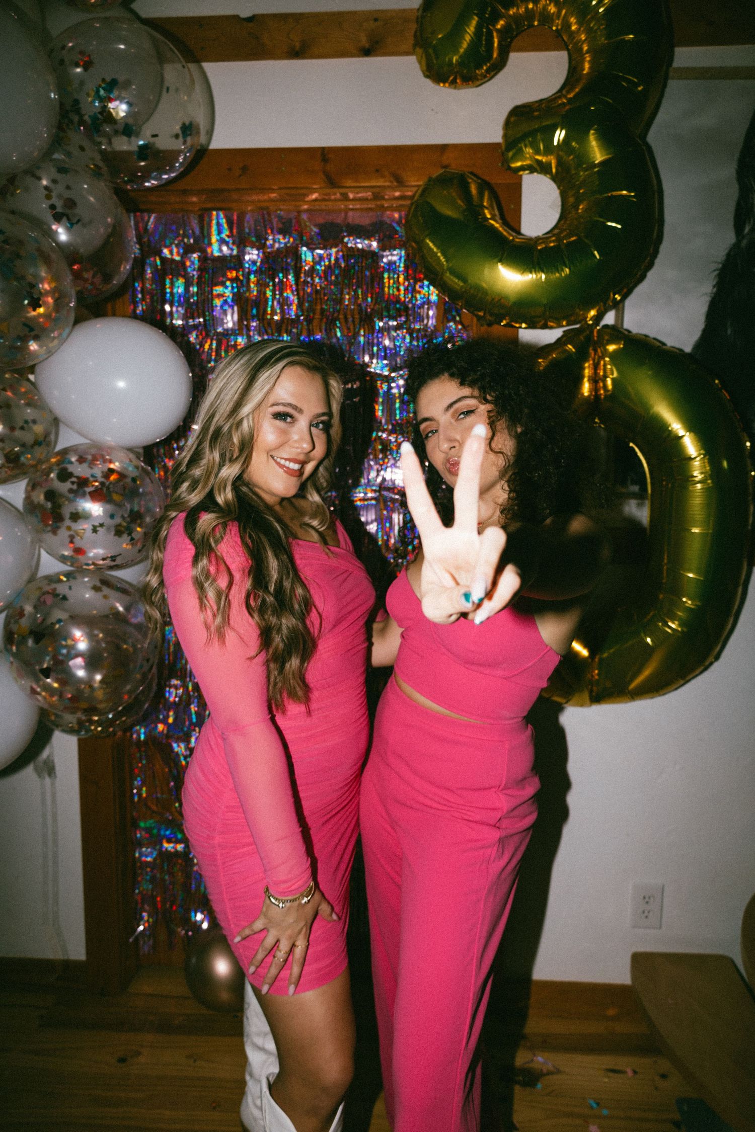 Two friends in pink dresses posing with balloons and a large gold number 3 decoration.