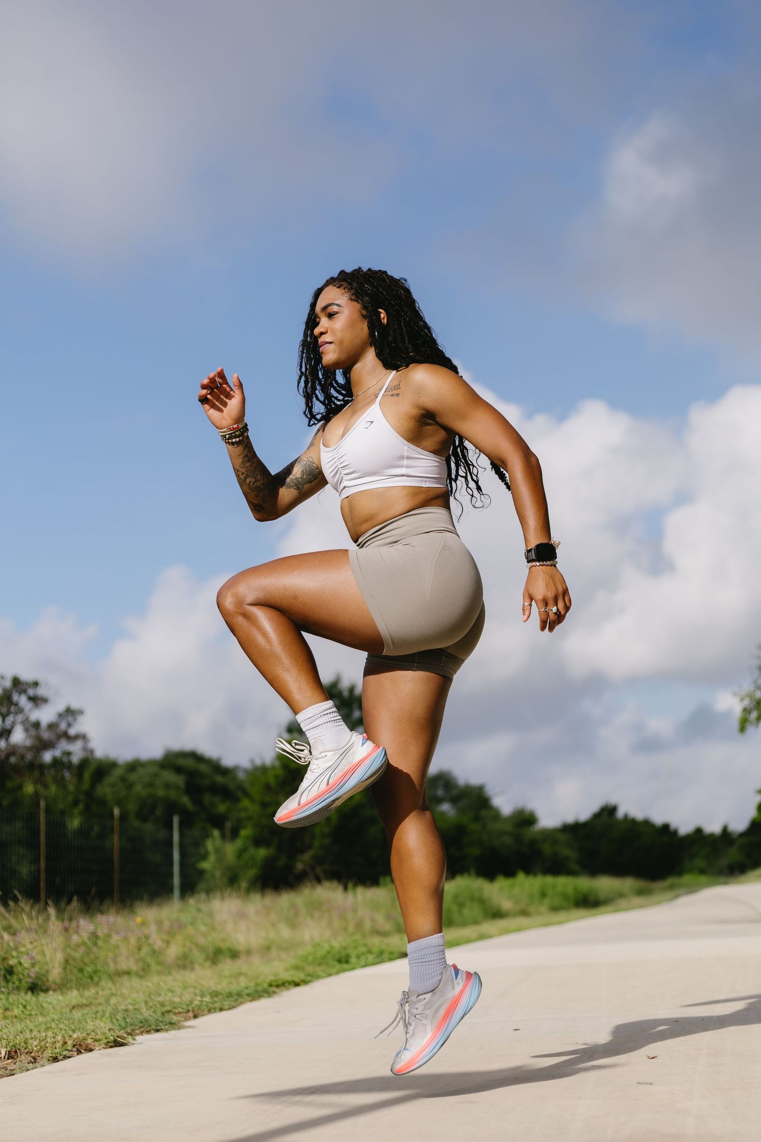 Athletic figure demonstrates dynamic stretching sequence on an outdoor path with blue sky and clouds in background.