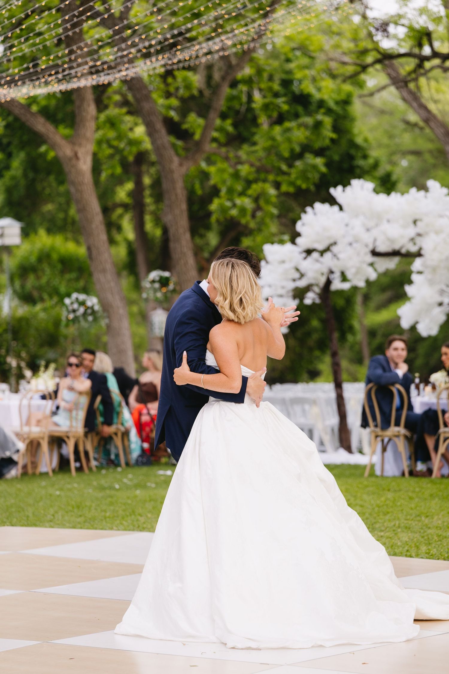 Bride and groom share their first dance outdoors at elegant garden wedding reception with white floral decorations.