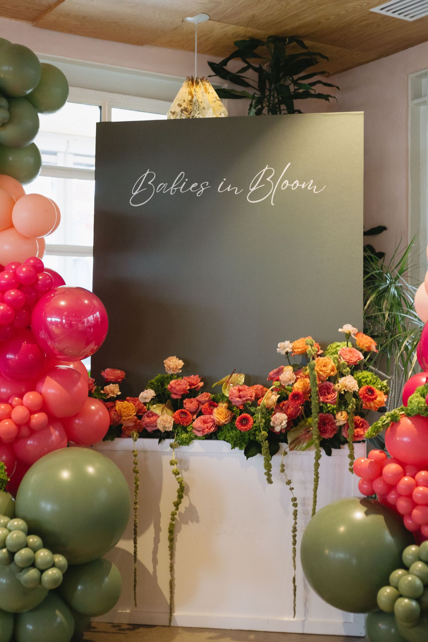 Dark backdrop with Babies in Bloom text, surrounded by pink and green balloon arch with colorful floral arrangement.