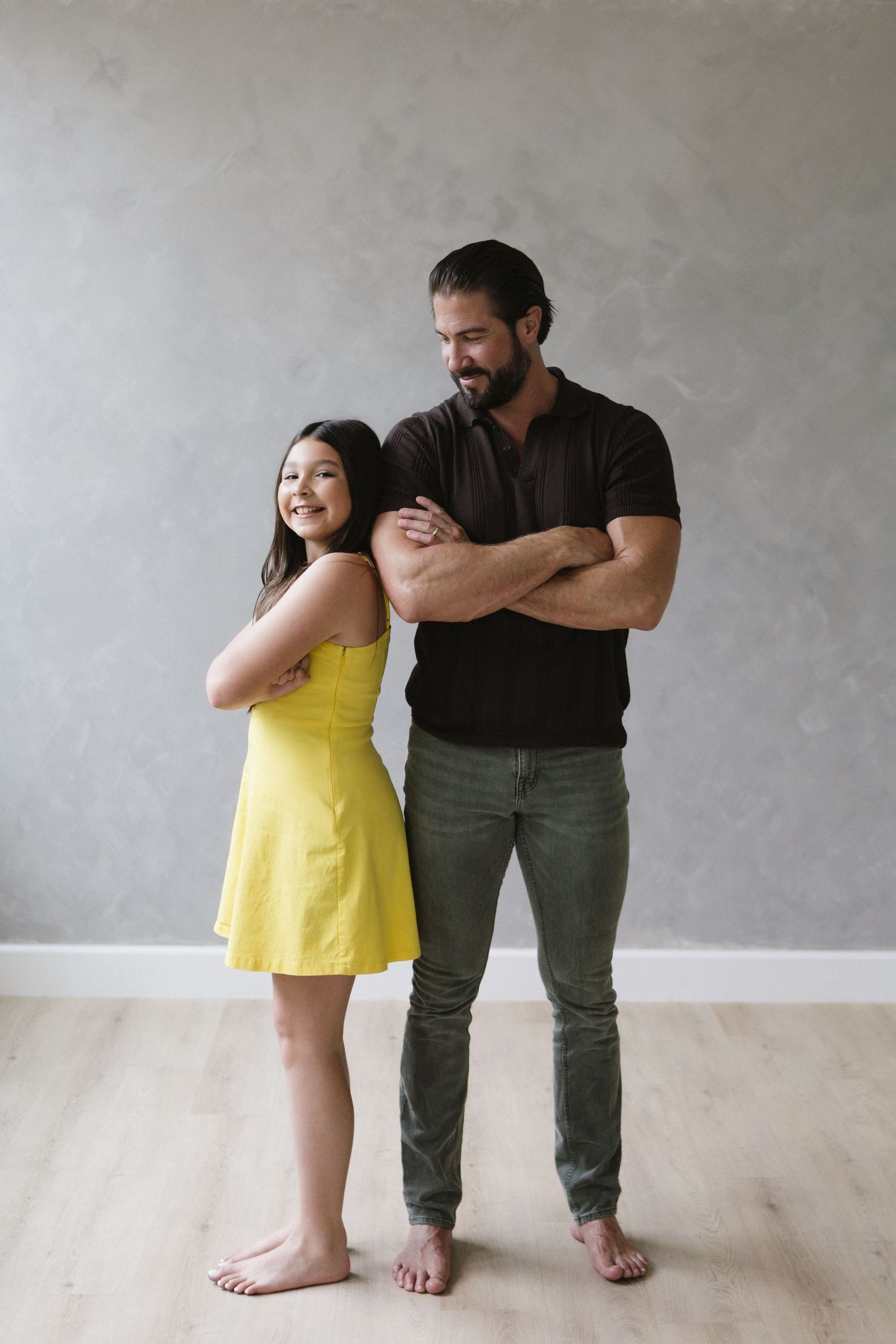 A casual portrait of two people posing with crossed arms against a minimalist gray backdrop.