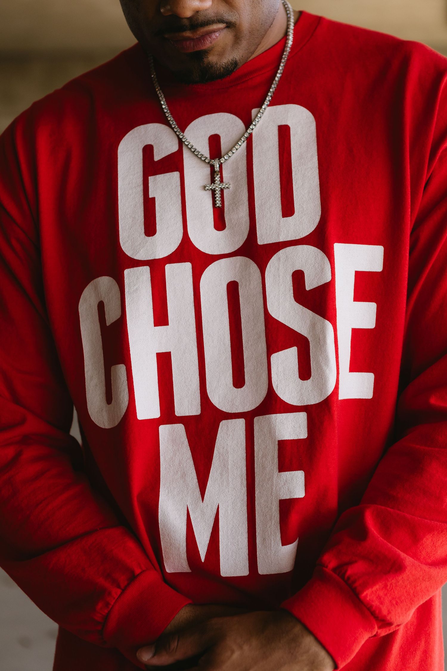 Man wearing red GOD CHOSE ME sweatshirt with cross necklace, close-up street style fashion photo.