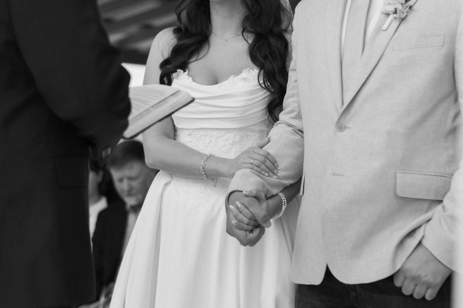 Black and white photo of bride and groom holding hands during outdoor wedding ceremony.