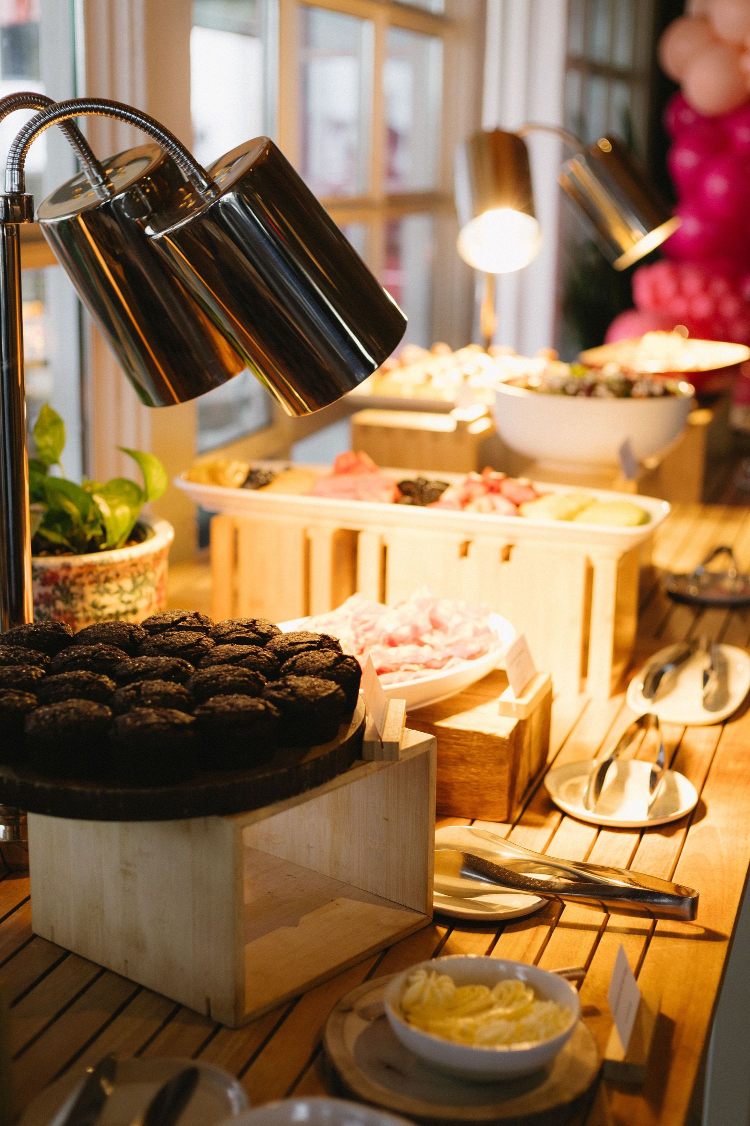 A warm buffet spread with chocolate cookies under a heat lamp, surrounded by wooden crates of assorted dishes and serving utensils.