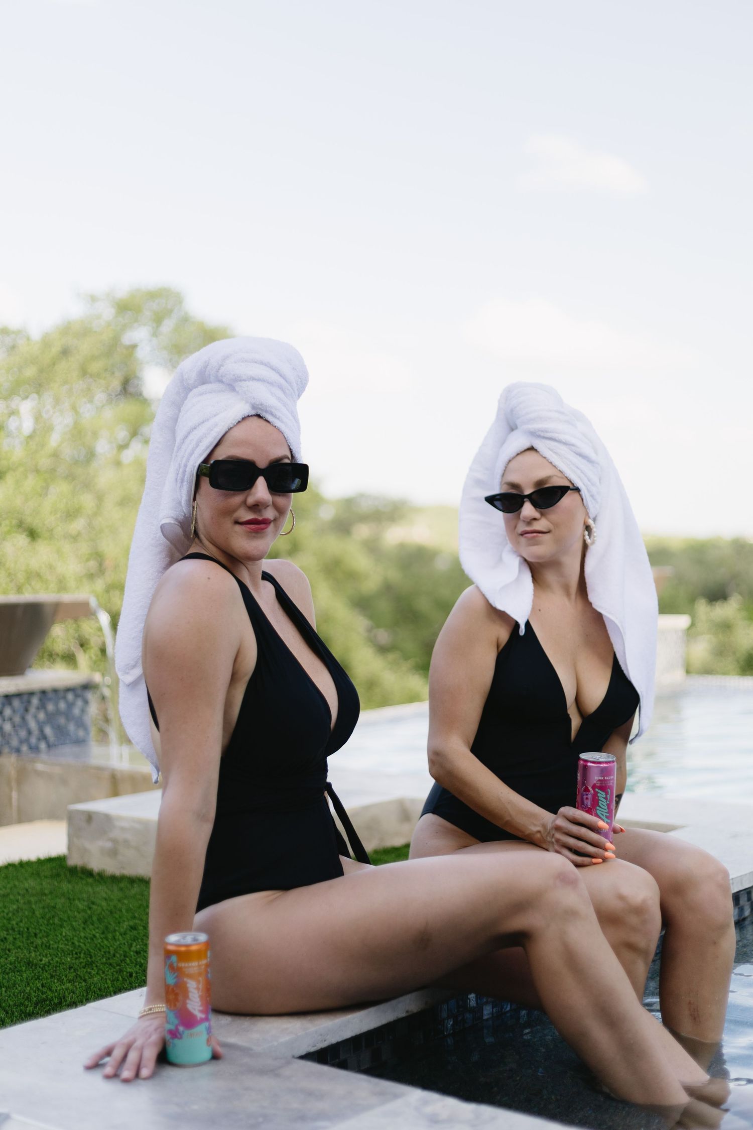 Friends in black swimsuits and white head wraps enjoying a poolside conversation.