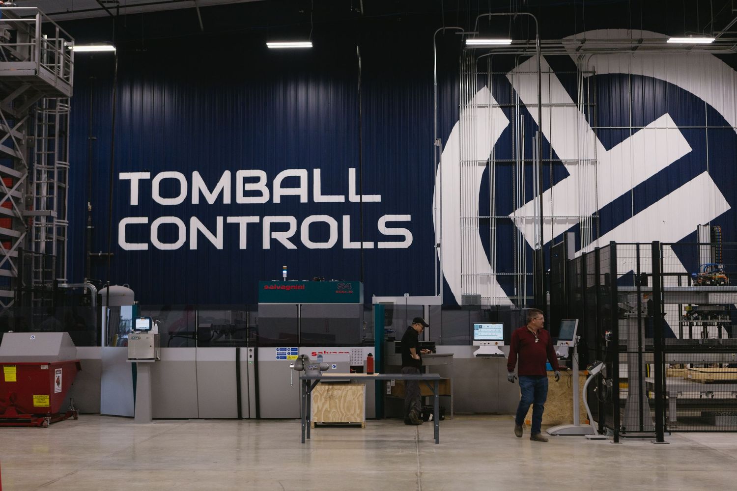 Industrial warehouse interior with large machinery and equipment visible under fluorescent lighting.