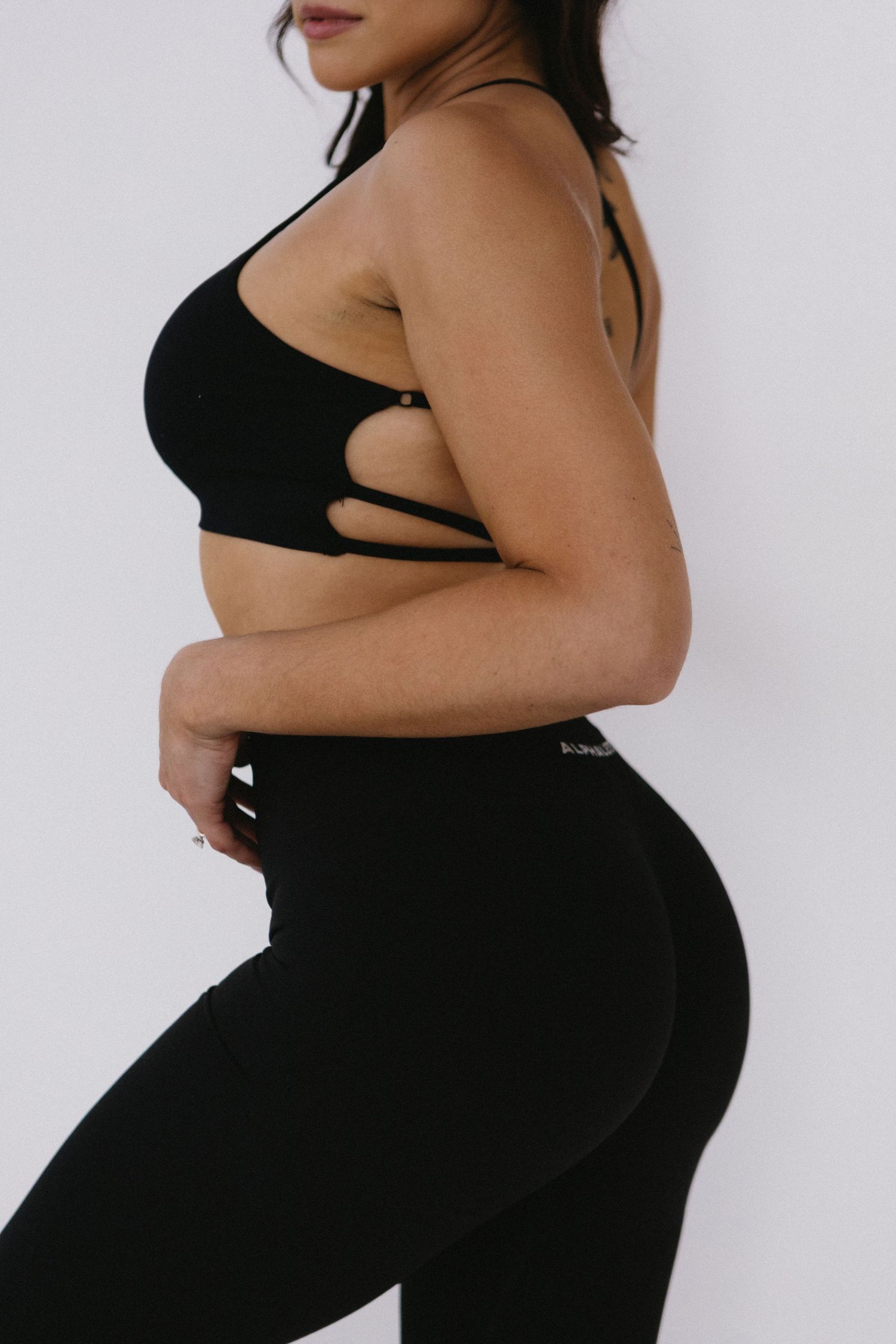 Woman wearing black strappy sports bra and high-waist leggings in side profile pose.