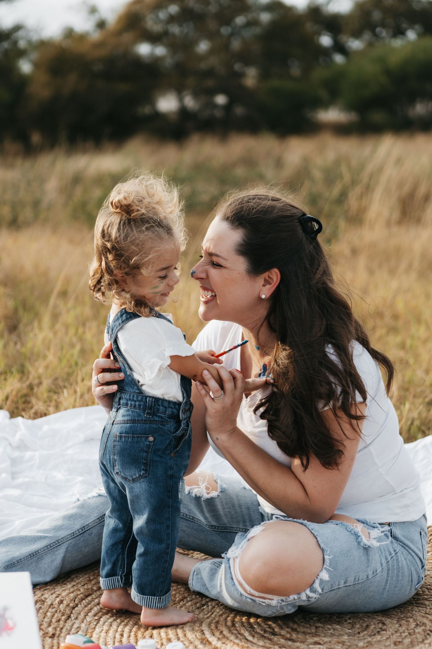 Mother and toddler sharing a joyful moment together on a blanket in a golden field during sunset.
