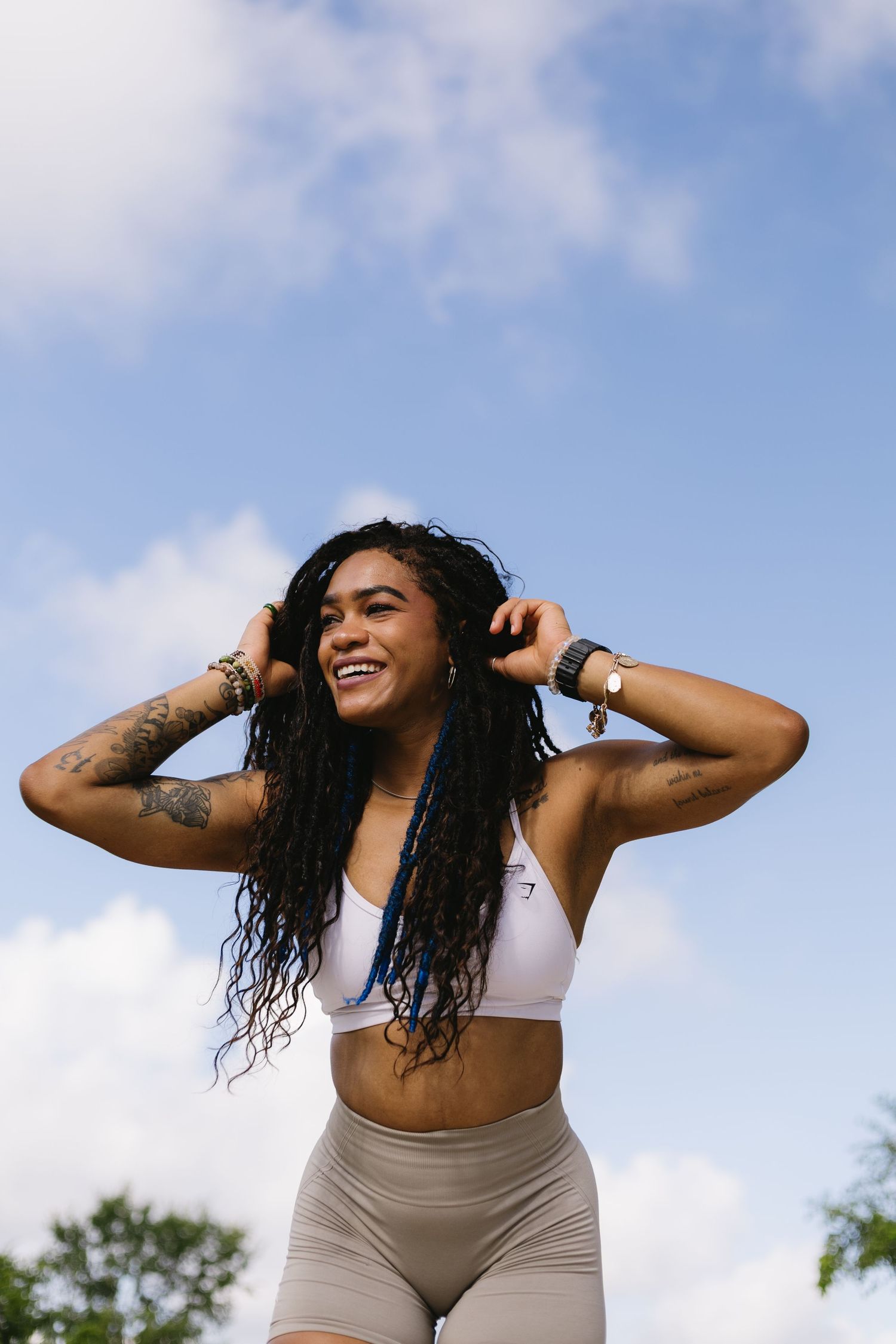 Woman in athletic wear dancing joyfully outdoors against a blue cloudy sky background.