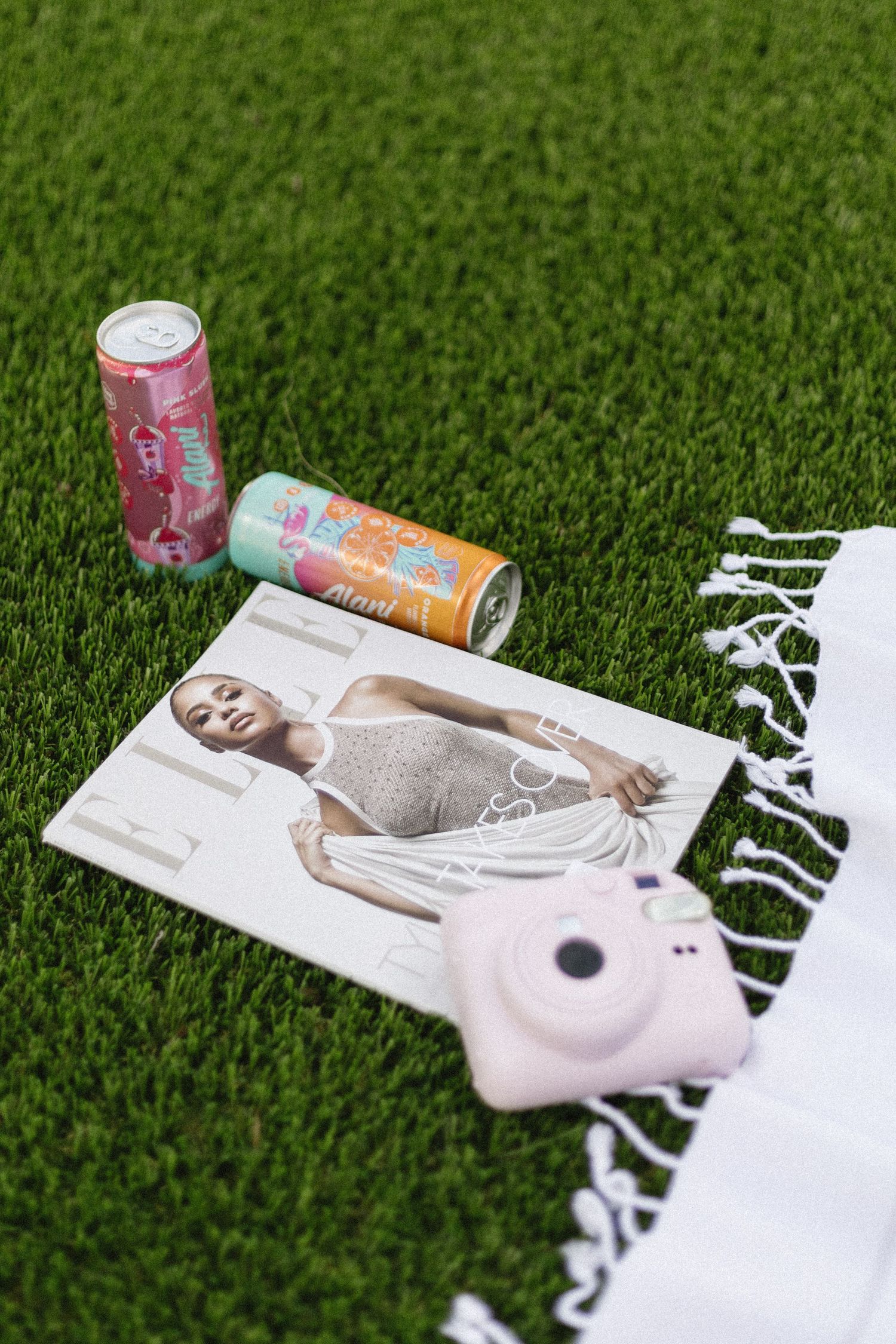 Empty beverage cans lying on a white towel placed on green grass lawn surface.