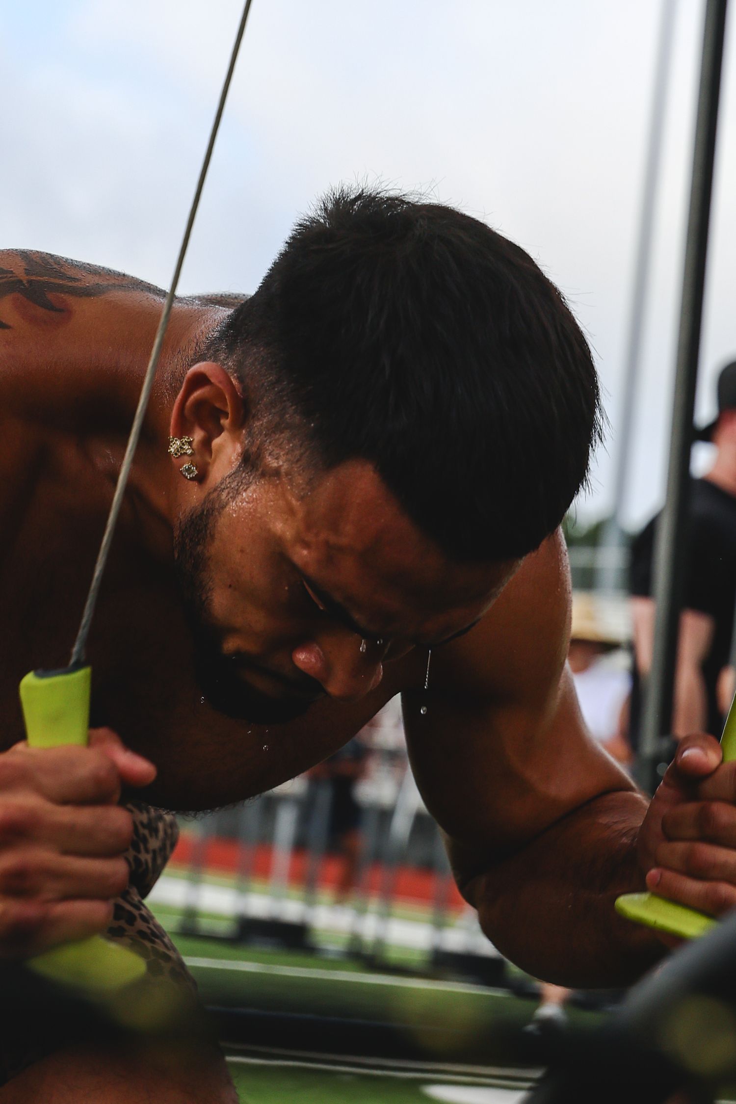 Muscular tattooed man with earrings straining during intense outdoor workout, sweating and focused.