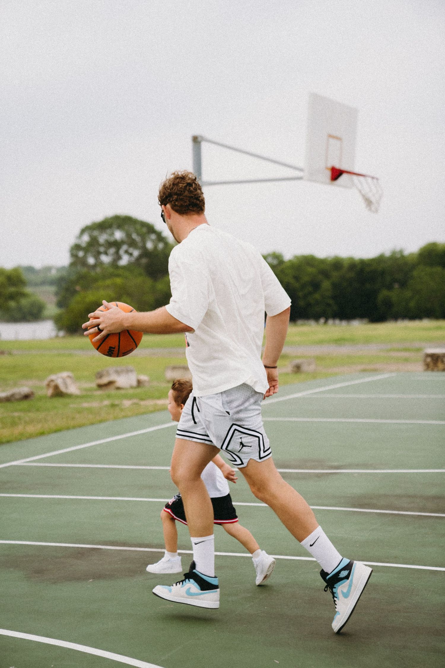 Man and child playing basketball on an outdoor court, with a hoop visible in the background.