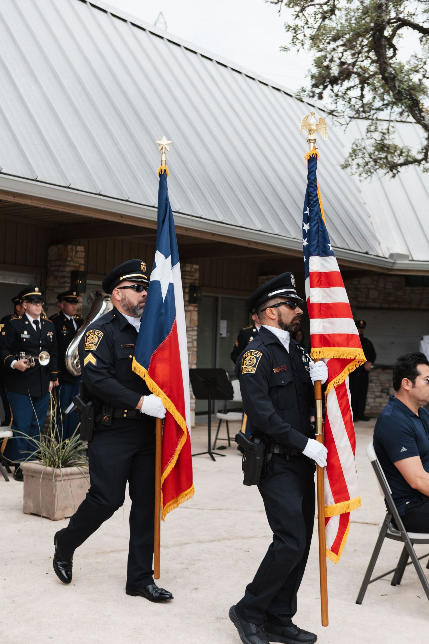Police officers in uniform carry Texas and American flags during an outdoor color guard ceremony.