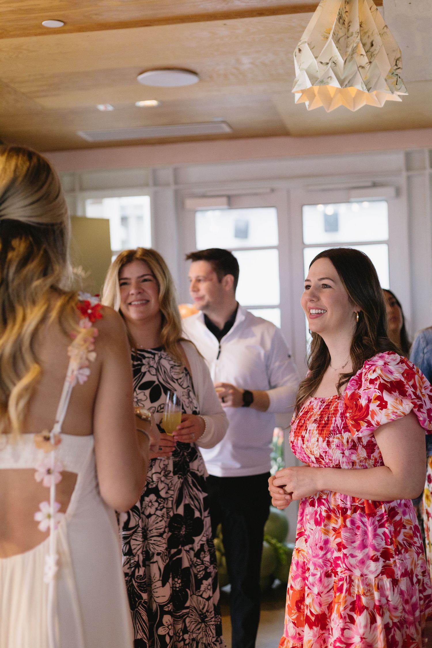 Guests in floral dresses smiling and socializing at an elegant indoor wedding reception event.