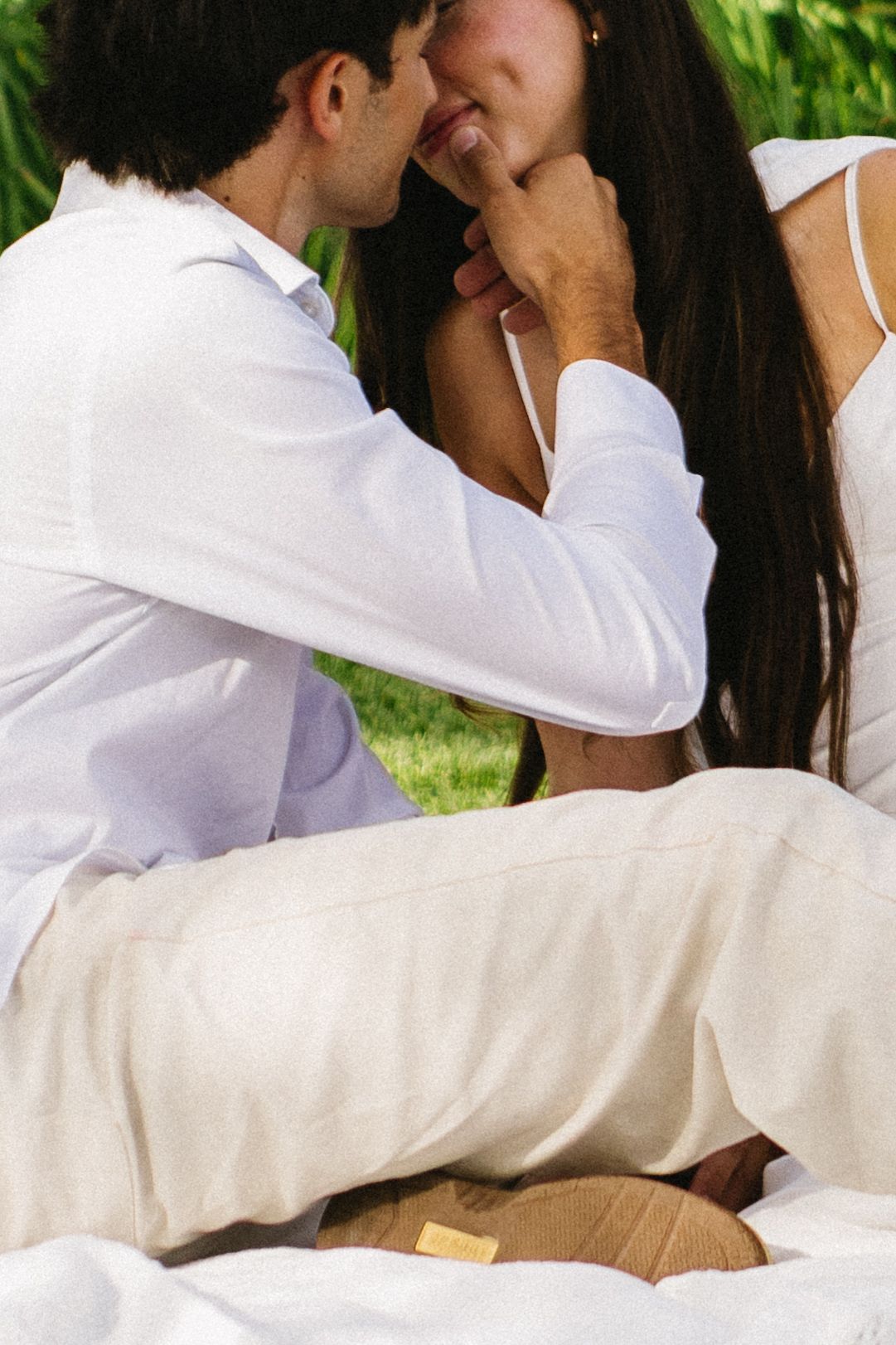 Romantic couple in white outfits sharing an intimate moment outdoors on a sunny day.