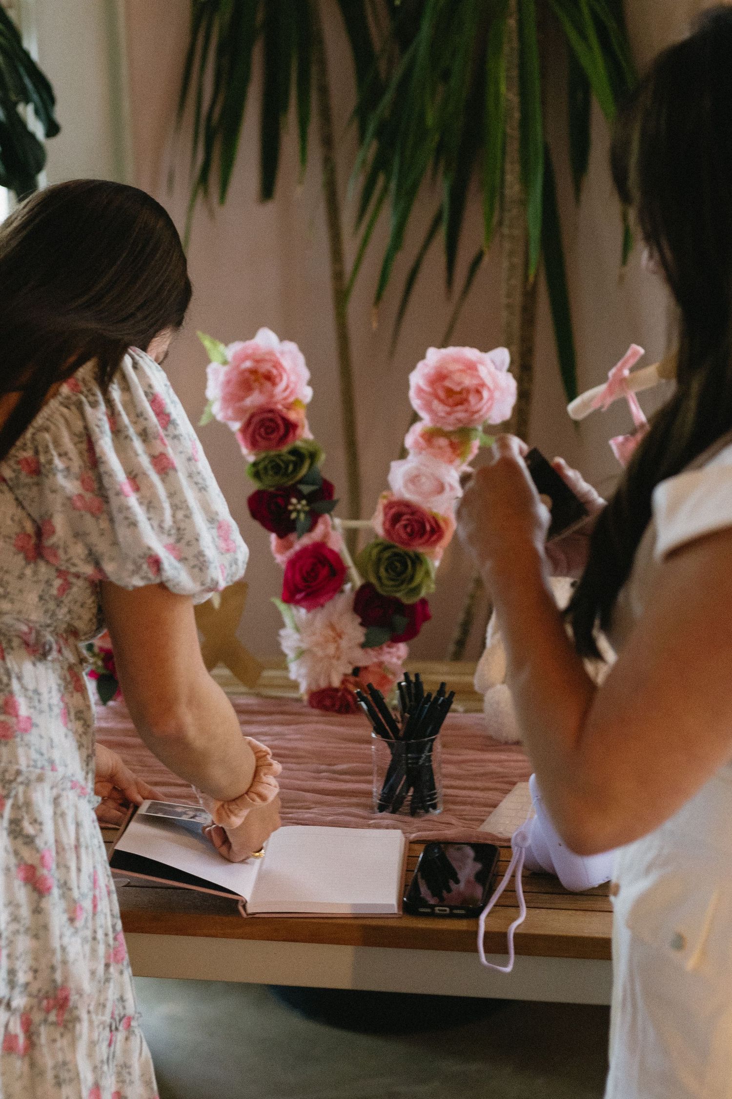 Two women arranging colorful pink and green floral decorations on a wooden table at an event.