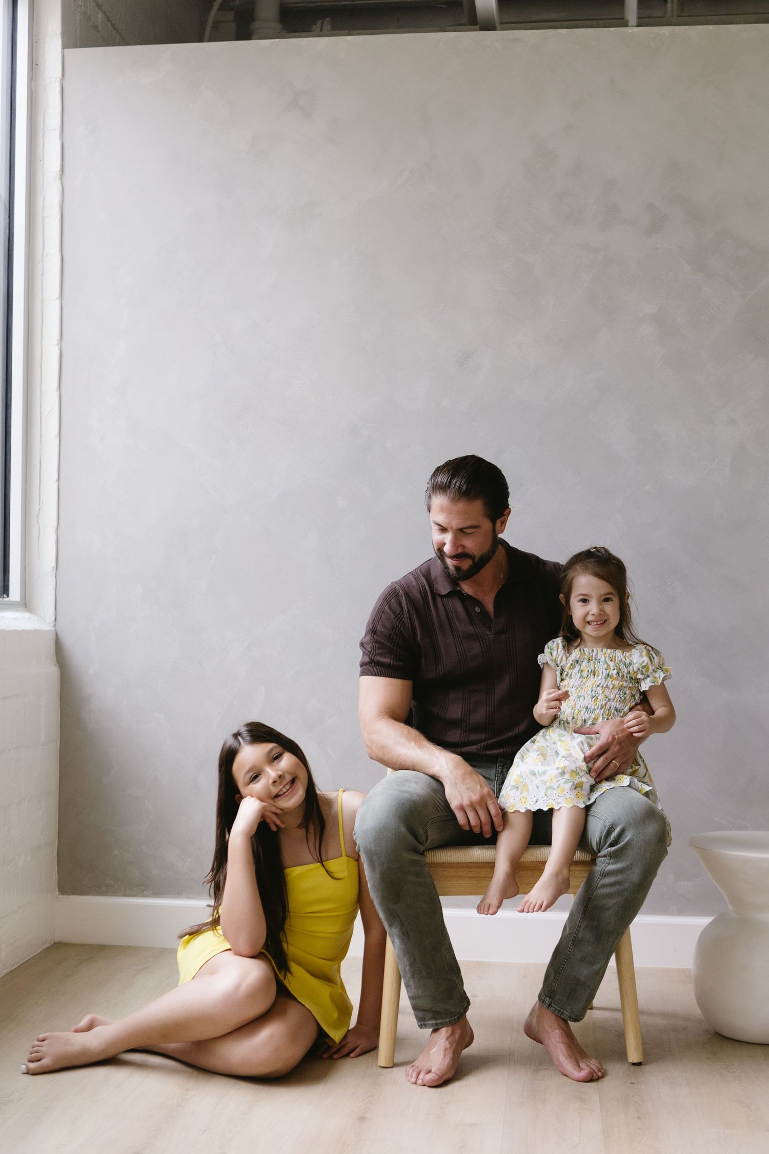 A family poses together in a minimalist setting with concrete walls and wooden furniture.