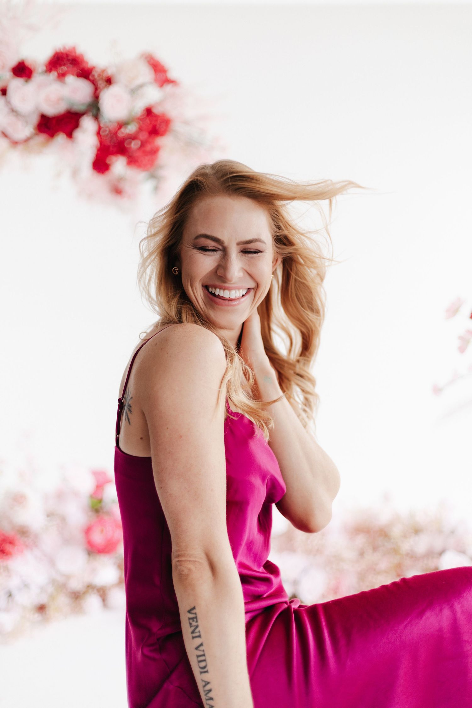 Person in magenta dress poses against white backdrop with pink floral decorations.