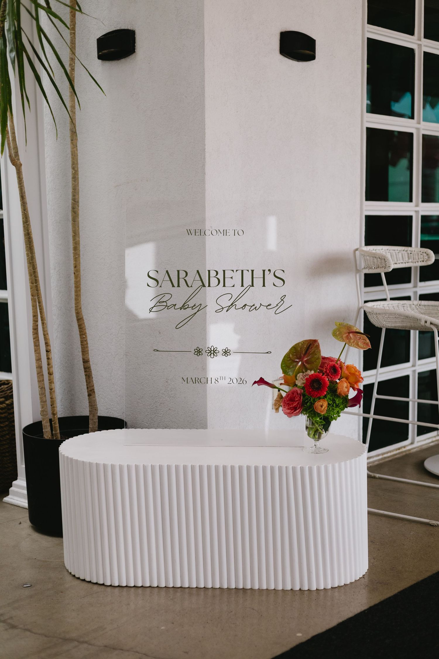 Elegant baby shower welcome sign for Sarabeth on a white fluted console table with colorful floral arrangement.