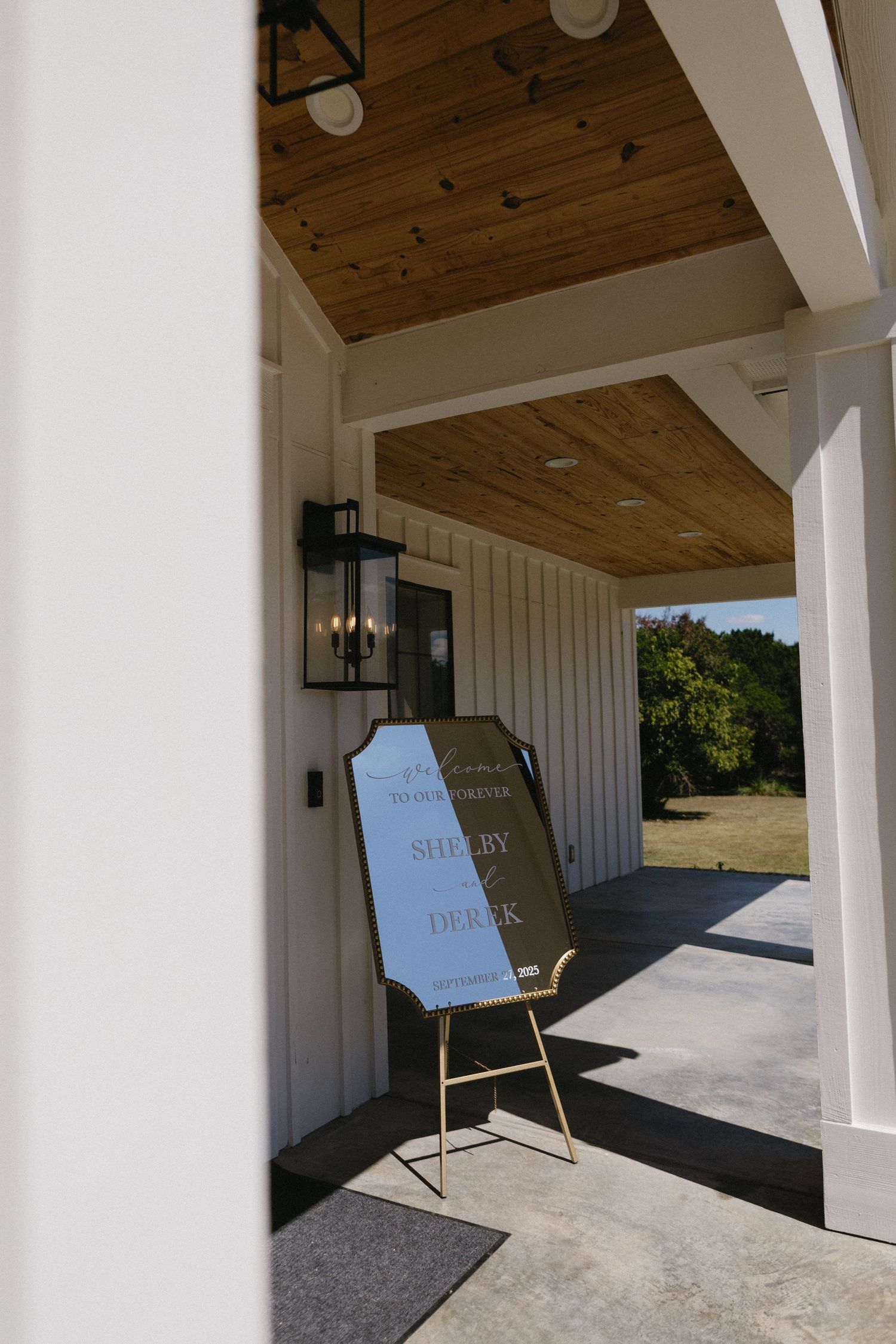 Modern white farmhouse exterior with wooden ceiling beams and concrete porch showcases directional signage.