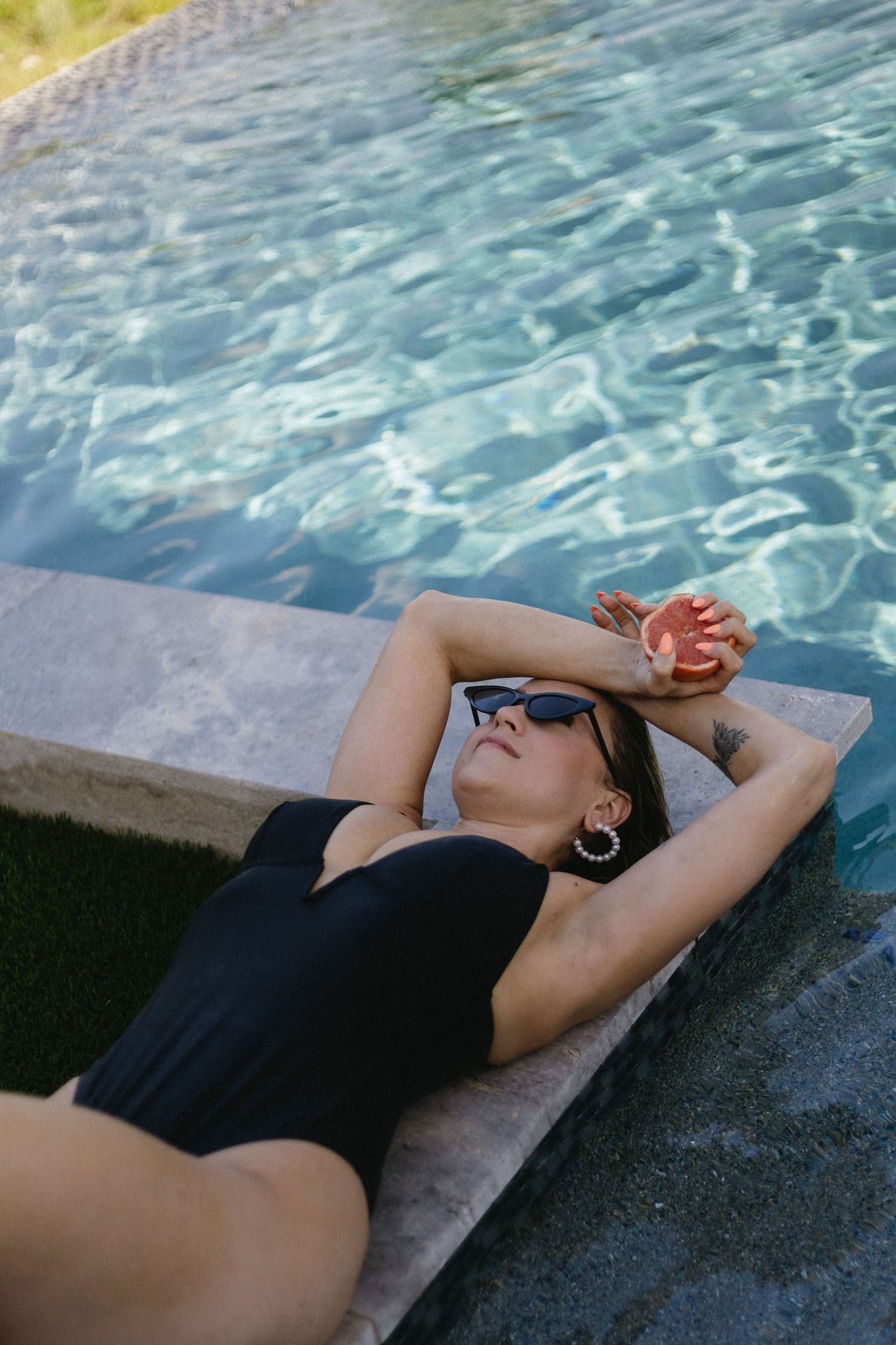 Person in black swimsuit relaxing by shimmering pool water on sunny day.