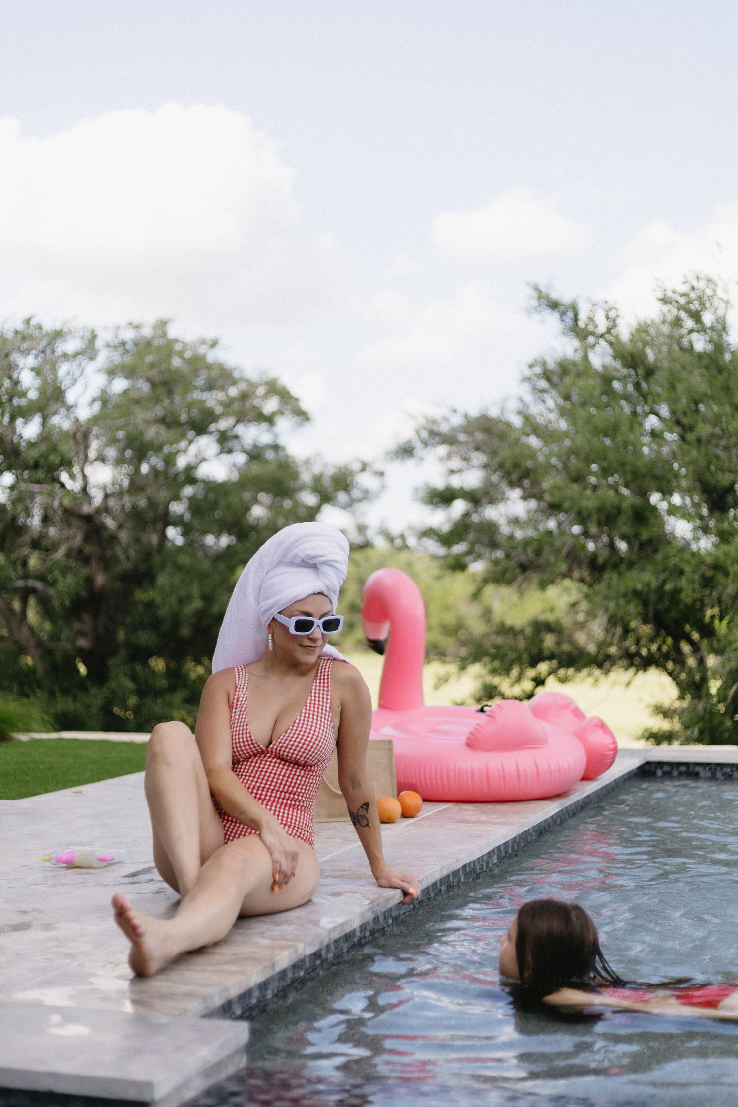 A person in a striped swimsuit lounges by a pool with a pink flamingo float on a summer day.