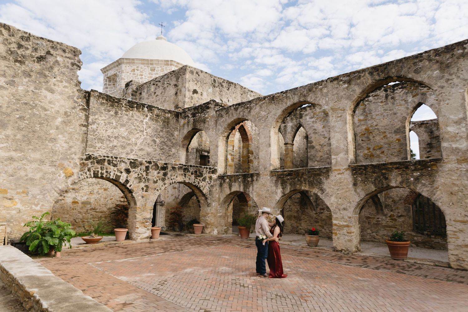 Couple embracing in the historic stone arched courtyard ruins of Mission San Jose in San Antonio, Texas.