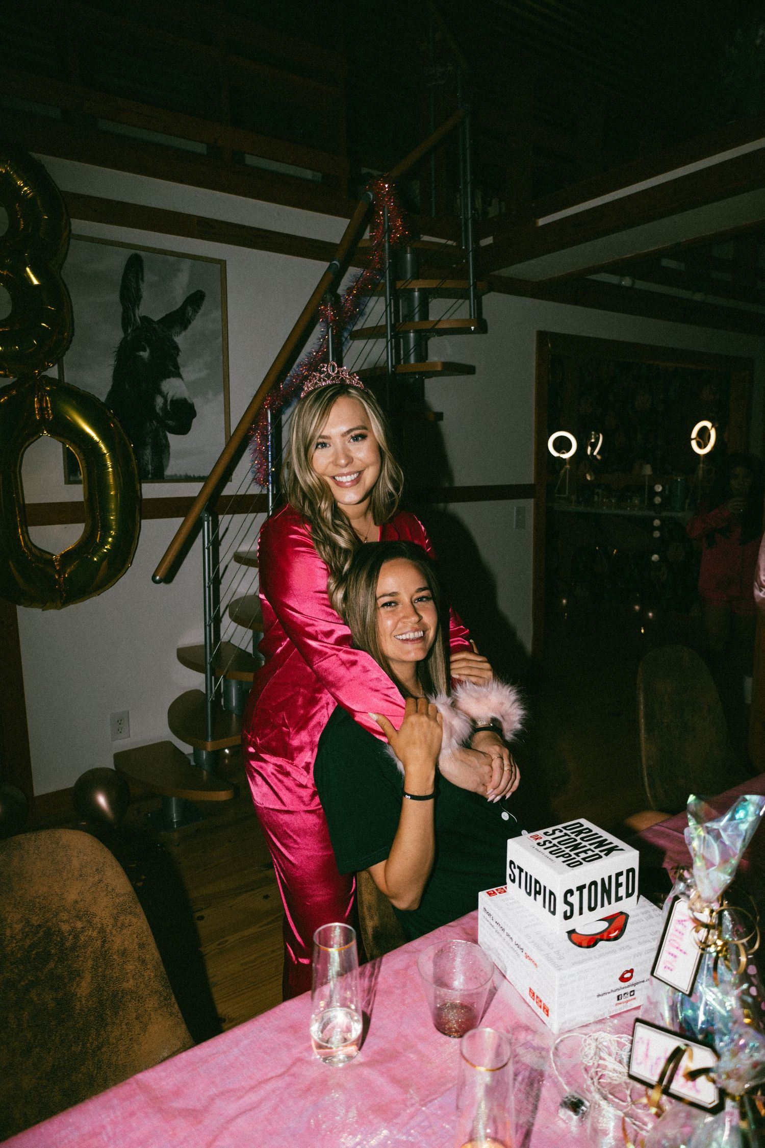 Friends having fun at party with pink decor and staircase in background.