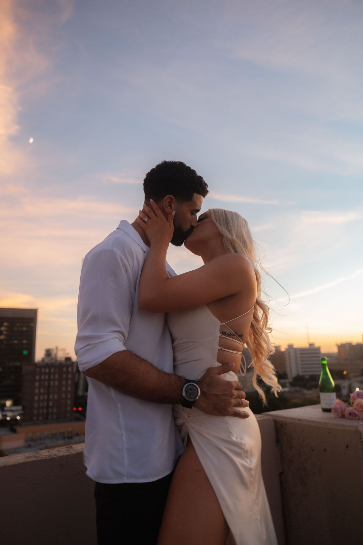 A romantic sunset moment shared between a couple on a rooftop overlooking a cityscape.