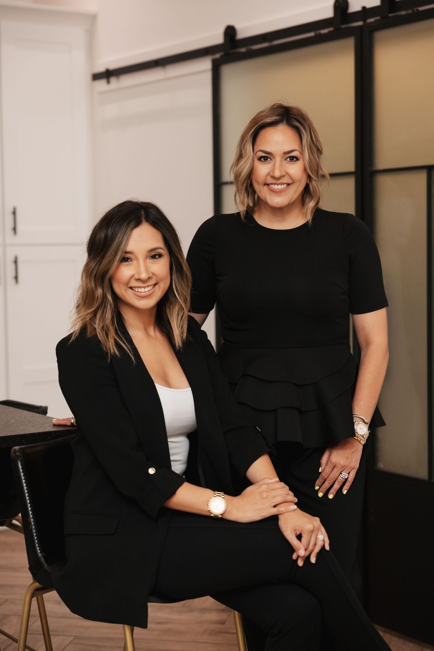 Indoor business photoshoot featuring two women in professional attire sharing genuine laughs.
