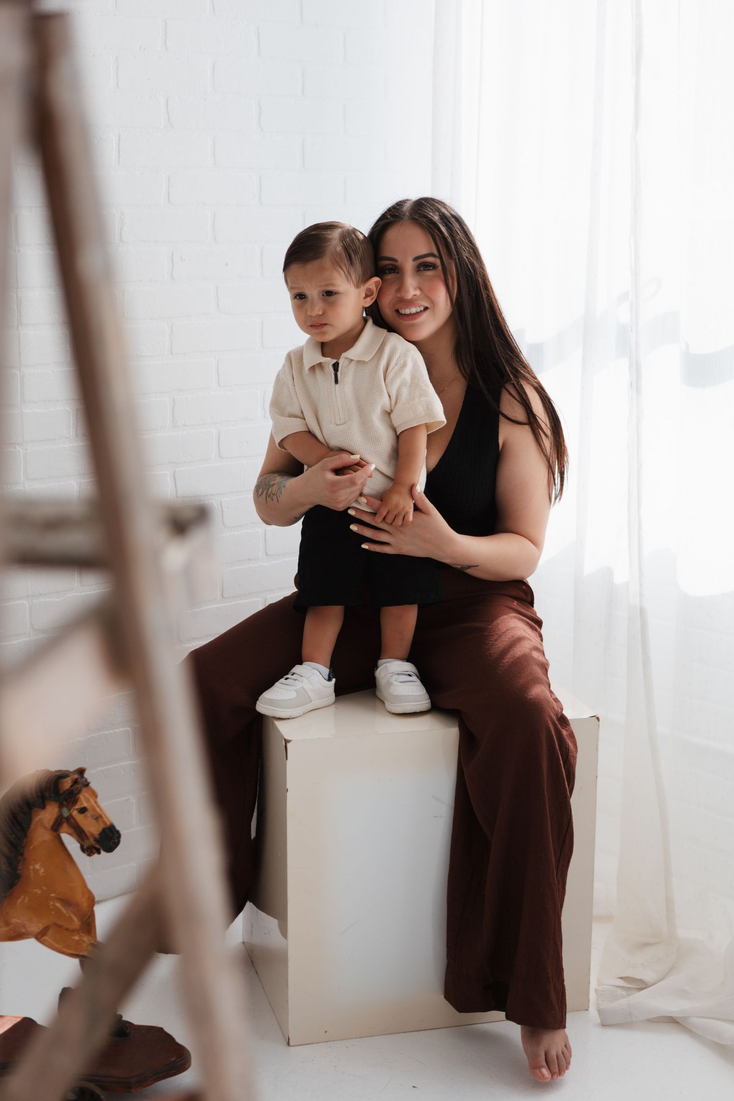 Three minimalist white studio portraits capture tender moments between two people in brown outfits while a cat observes.