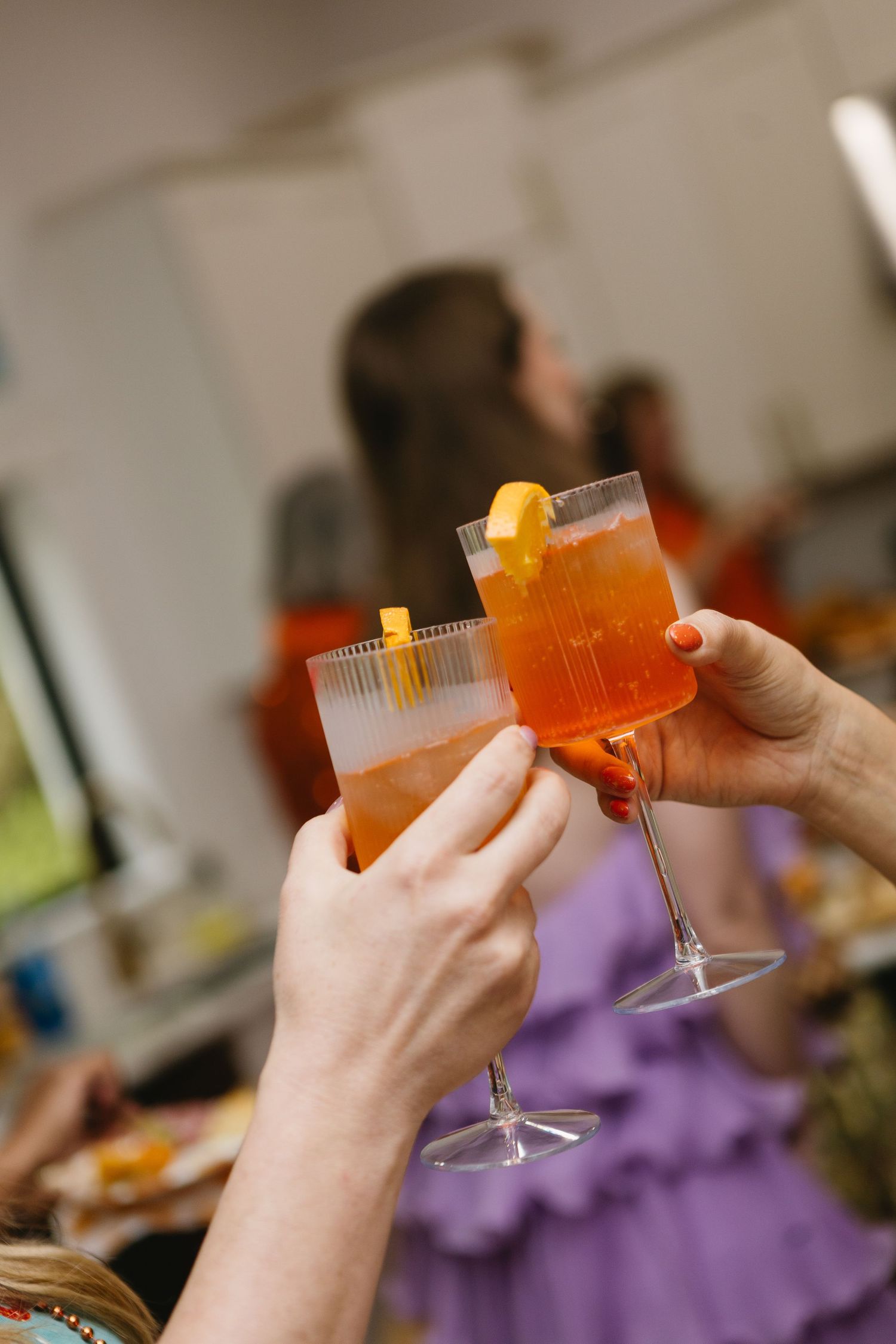 Several hands raise orange cocktails in plastic cups for a celebratory toast against a blurred background.
