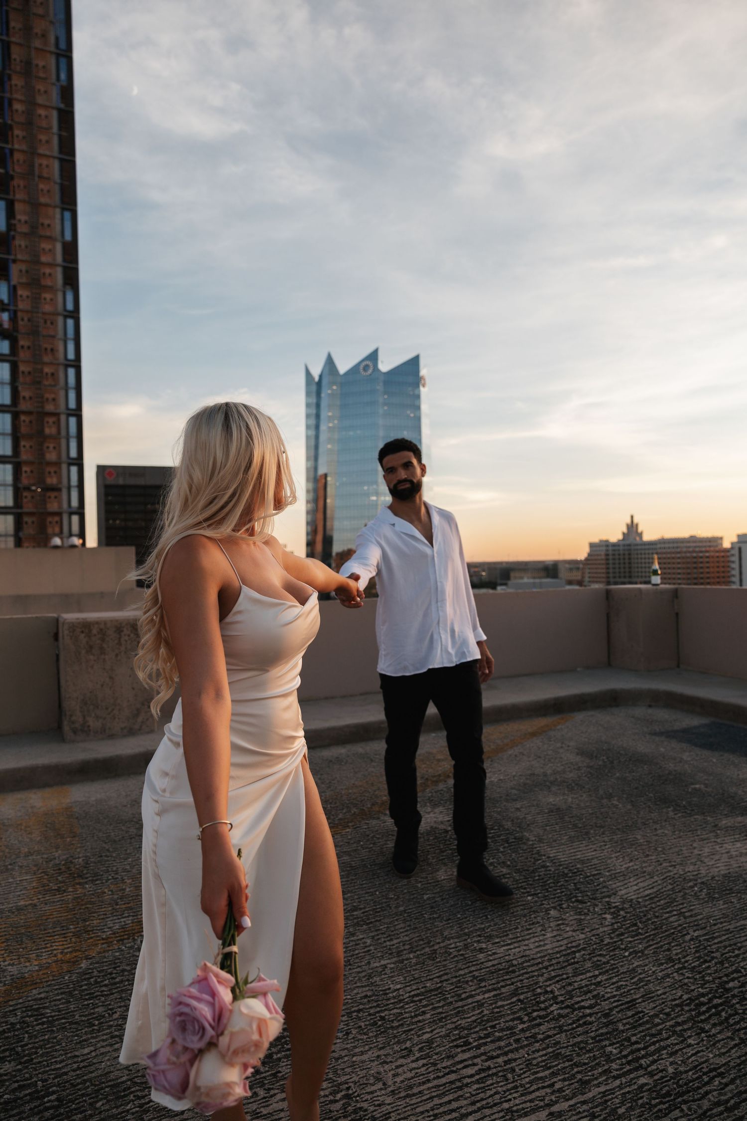 A couple shares a romantic moment on a rooftop with city buildings in the background.
