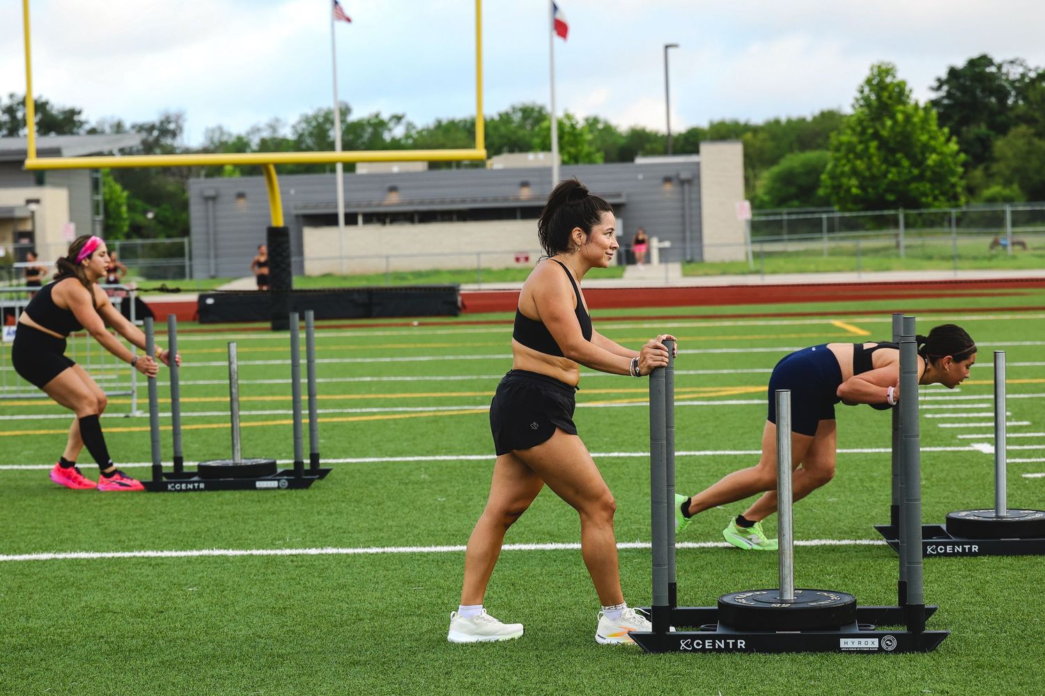 Athletes push weighted sleds across a football field turf during an outdoor group fitness training session.