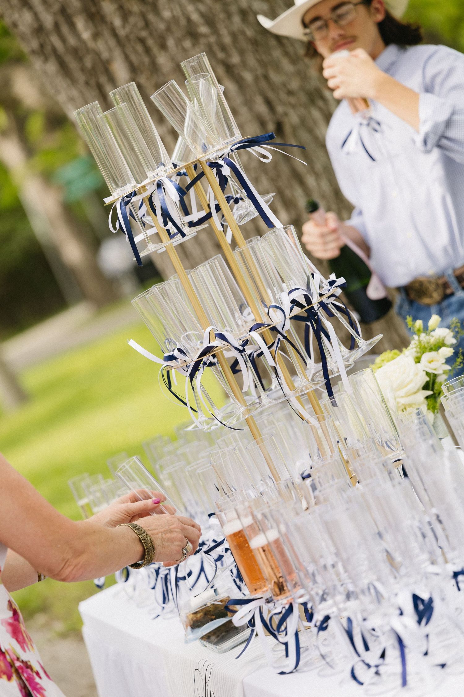 Champagne tower with navy blue ribbons at an outdoor wedding reception with guests serving themselves.