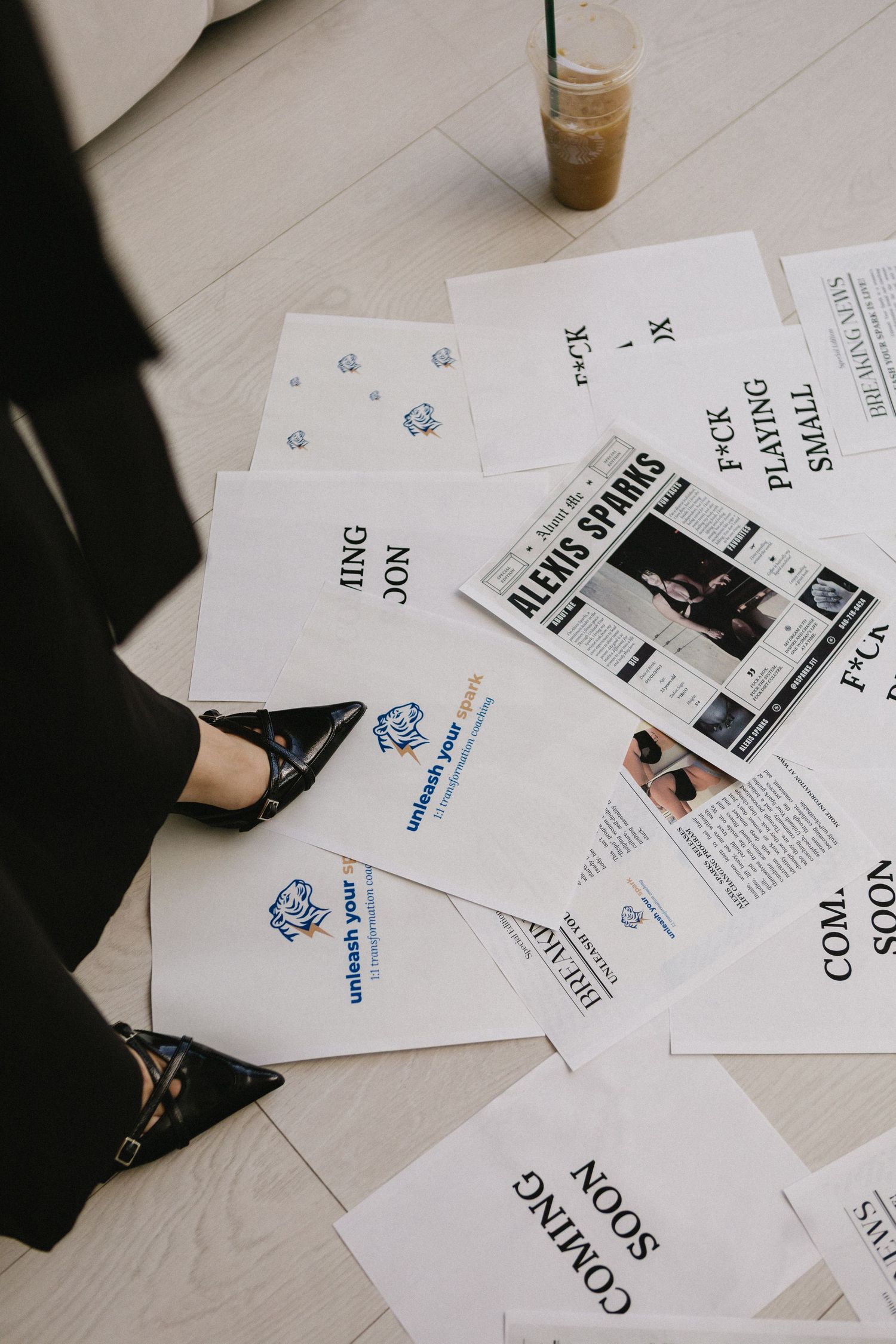 Papers spread on floor featuring Alexis Sparks branding, coming soon announcements, and motivational text beside black heeled shoes.