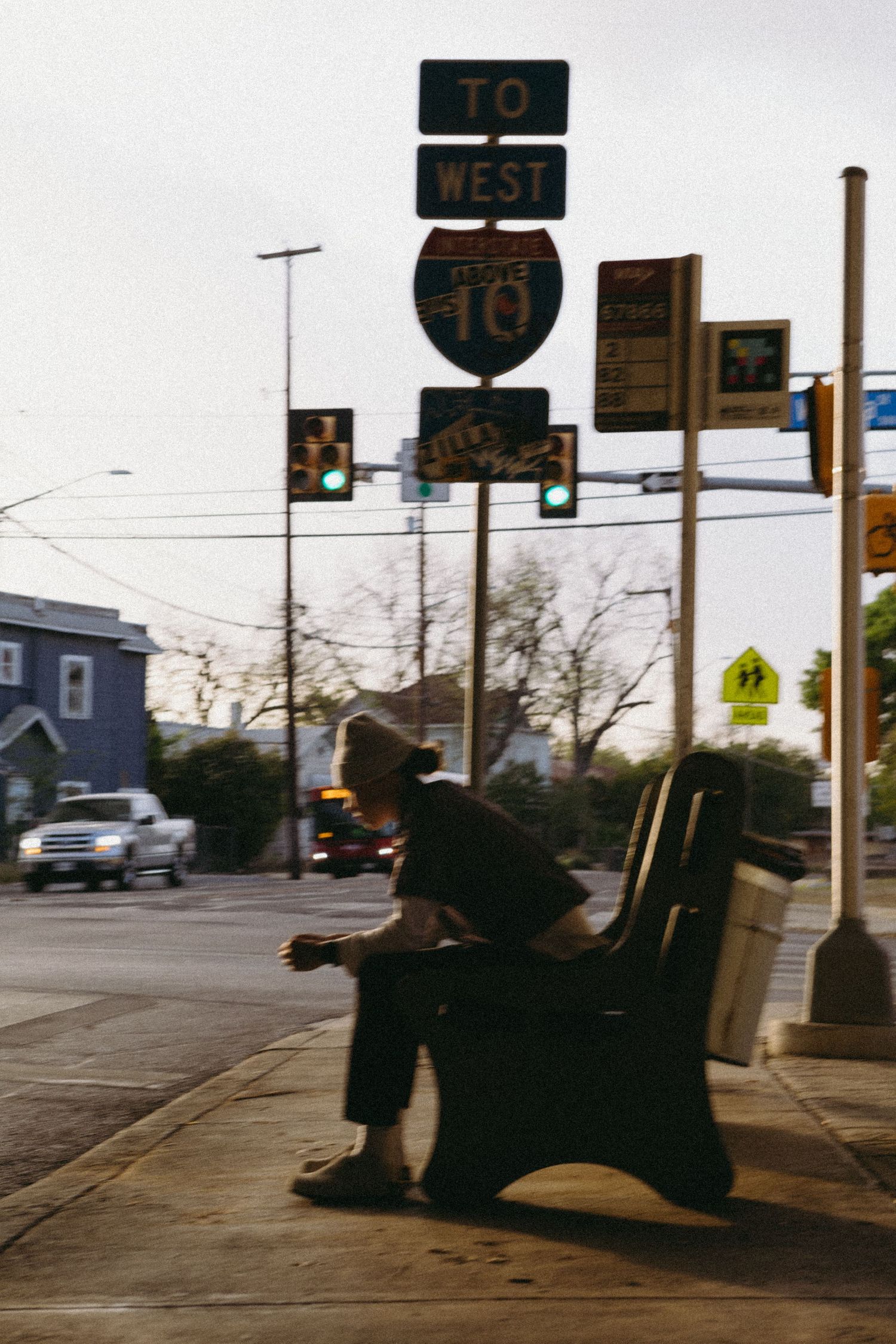 Person sitting alone on a bench near Interstate 10 West highway signs at a city intersection.