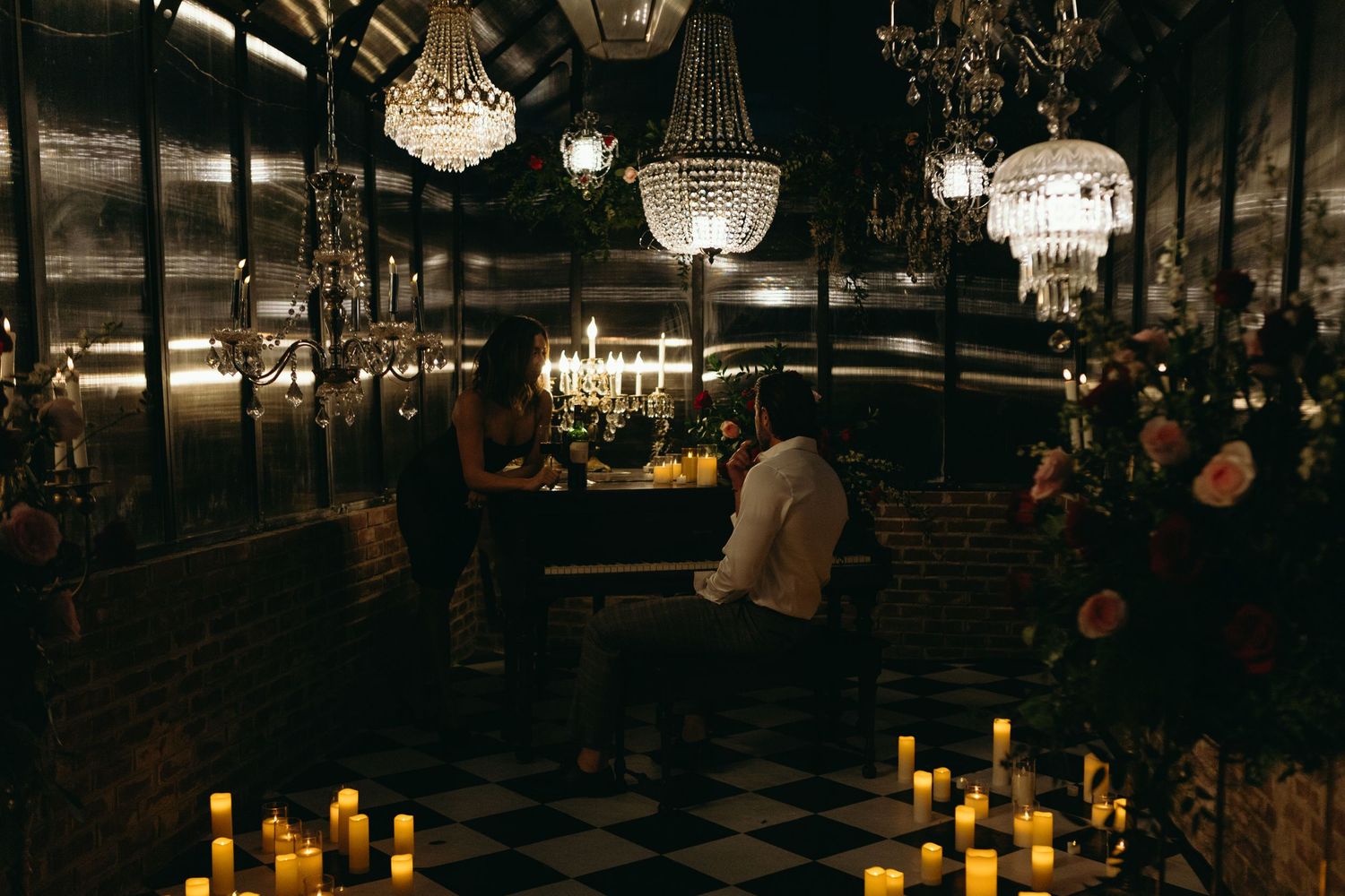 Romantic candlelit dinner for two in an elegant dark restaurant with crystal chandeliers and checkered floors.