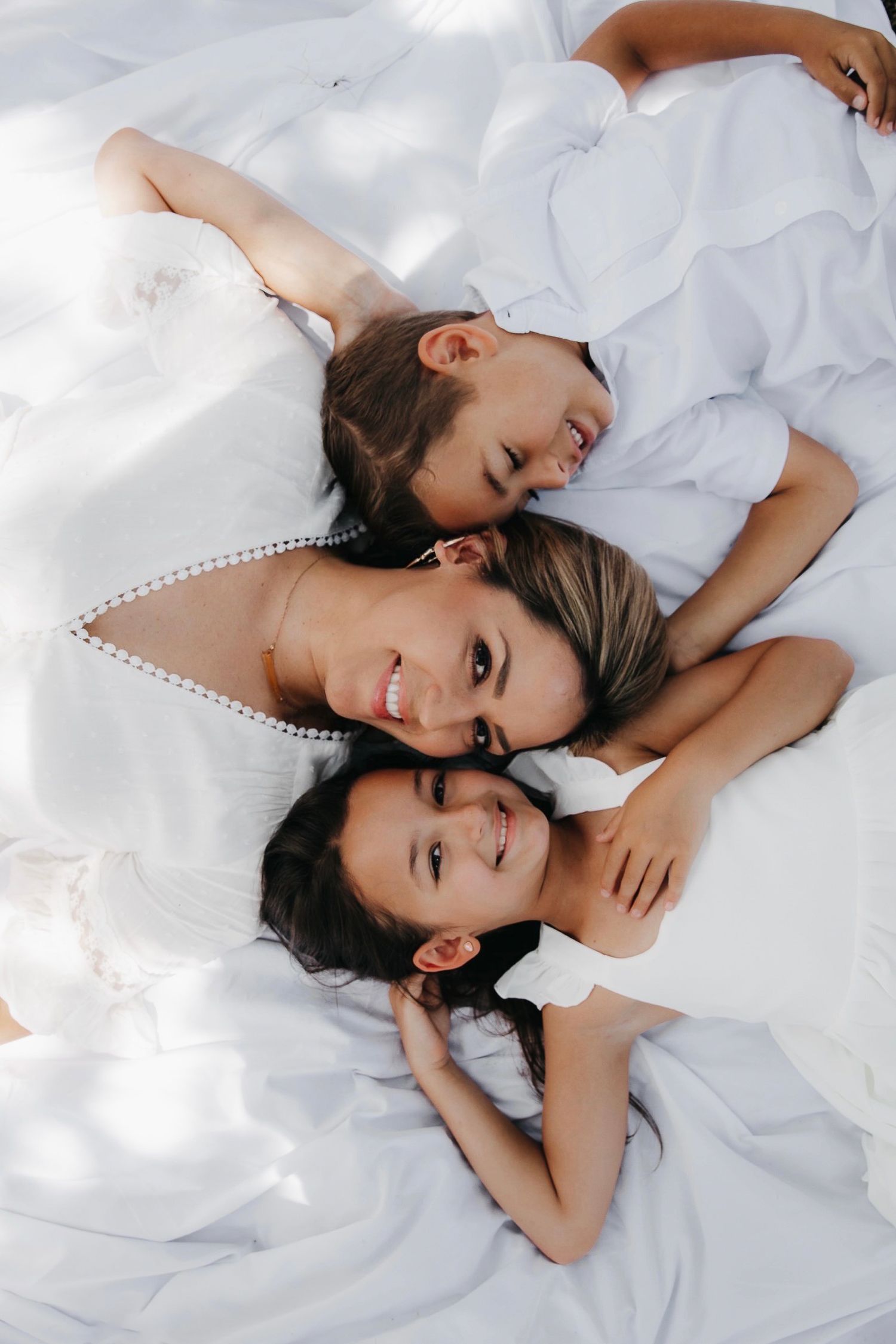 Two people lying on white bedding while laughing and taking playful photos together.