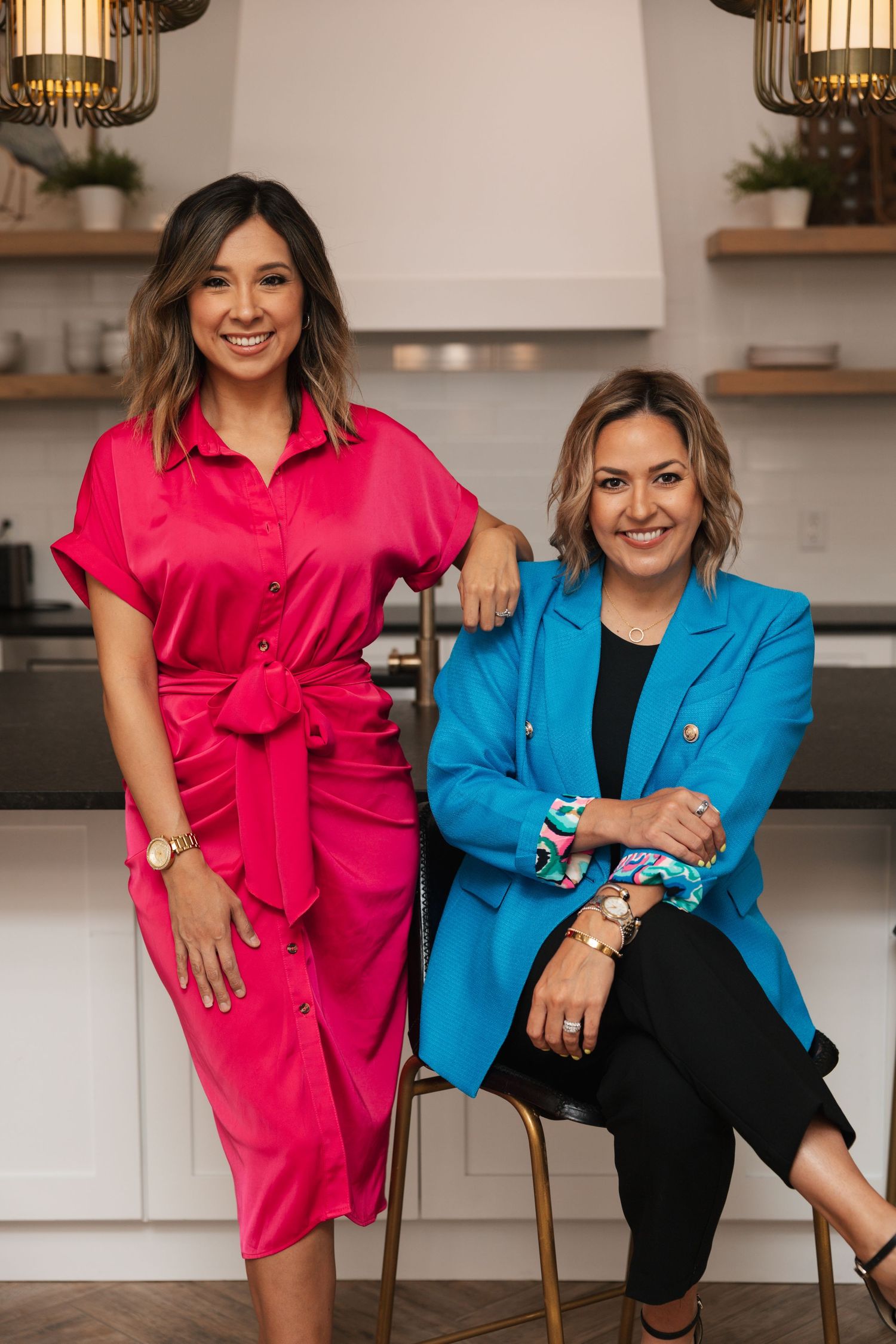 Professional duo in contrasting pink and blue outfits posing in modern office setting.