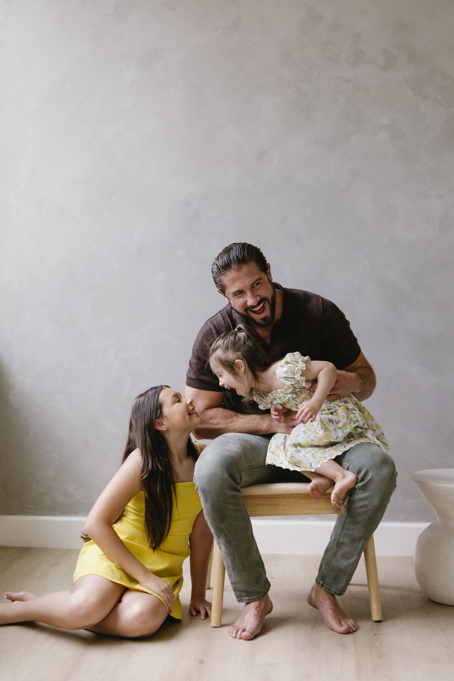 A heartwarming family moment captured against a minimalist gray wall background.